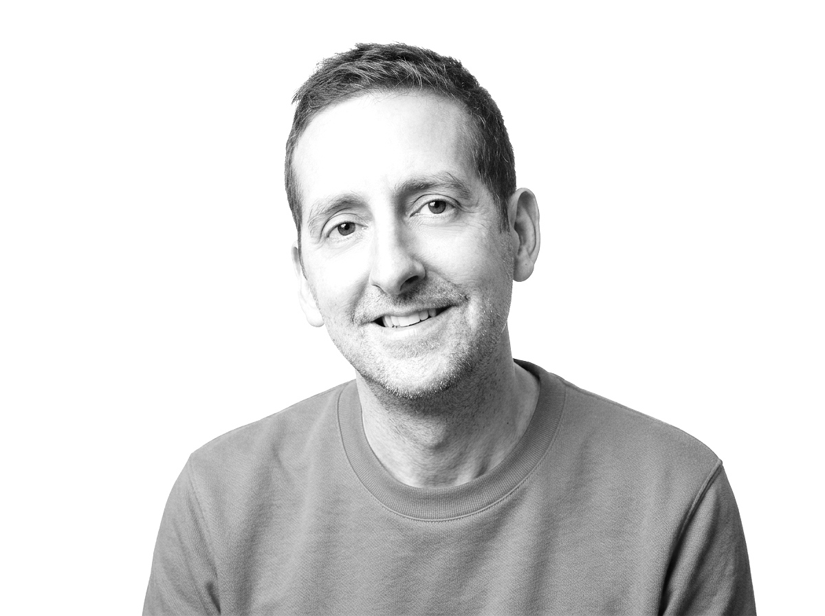 Black-and-white head-and-shoulders portrait of a smiling man in a crew-neck shirt against a white background
