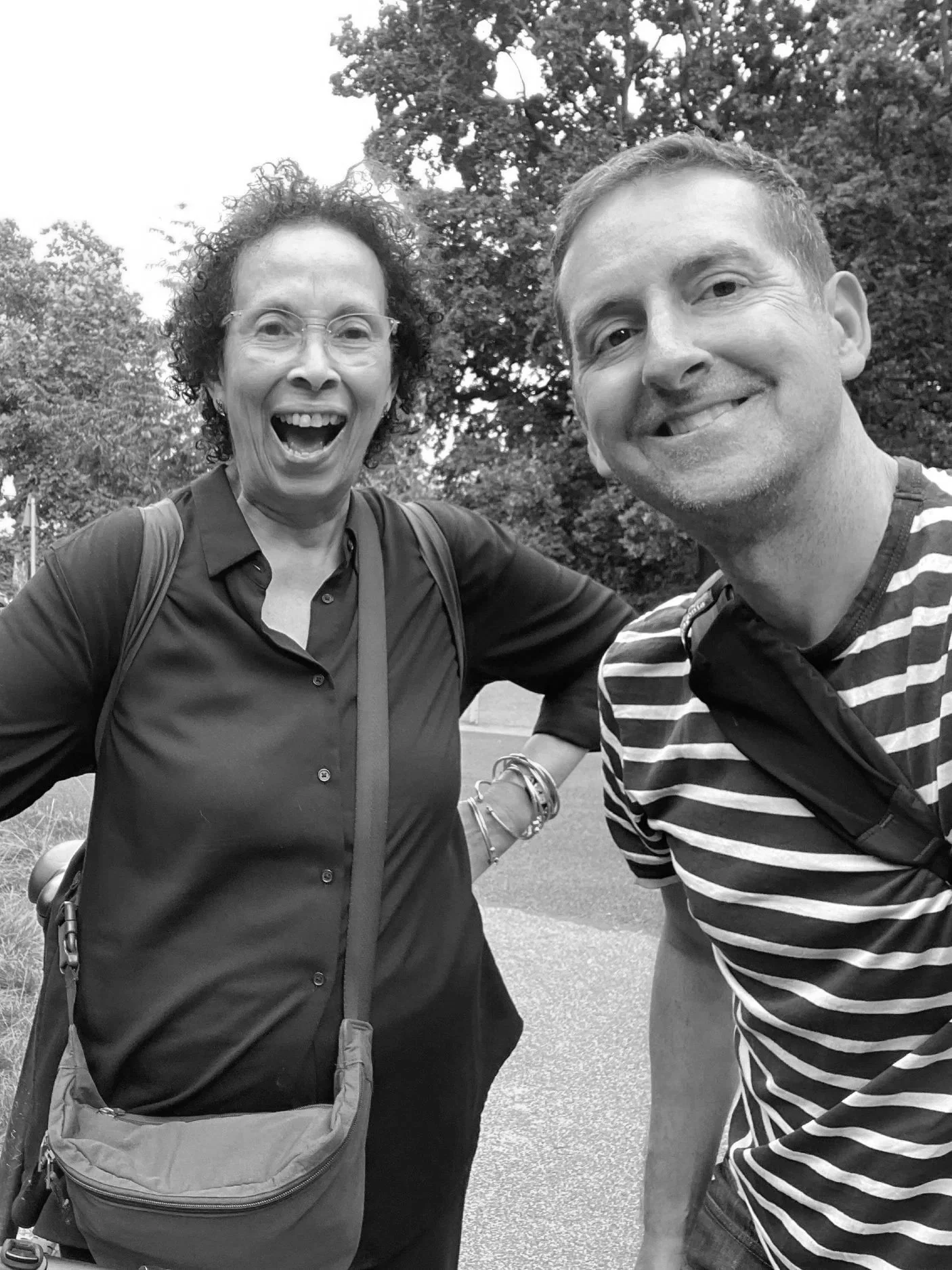 Black-and-white selfie of two smiling adults outdoors, with trees in the background.