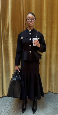 Woman in black outfit with glasses taking a selfie in front of gold curtain