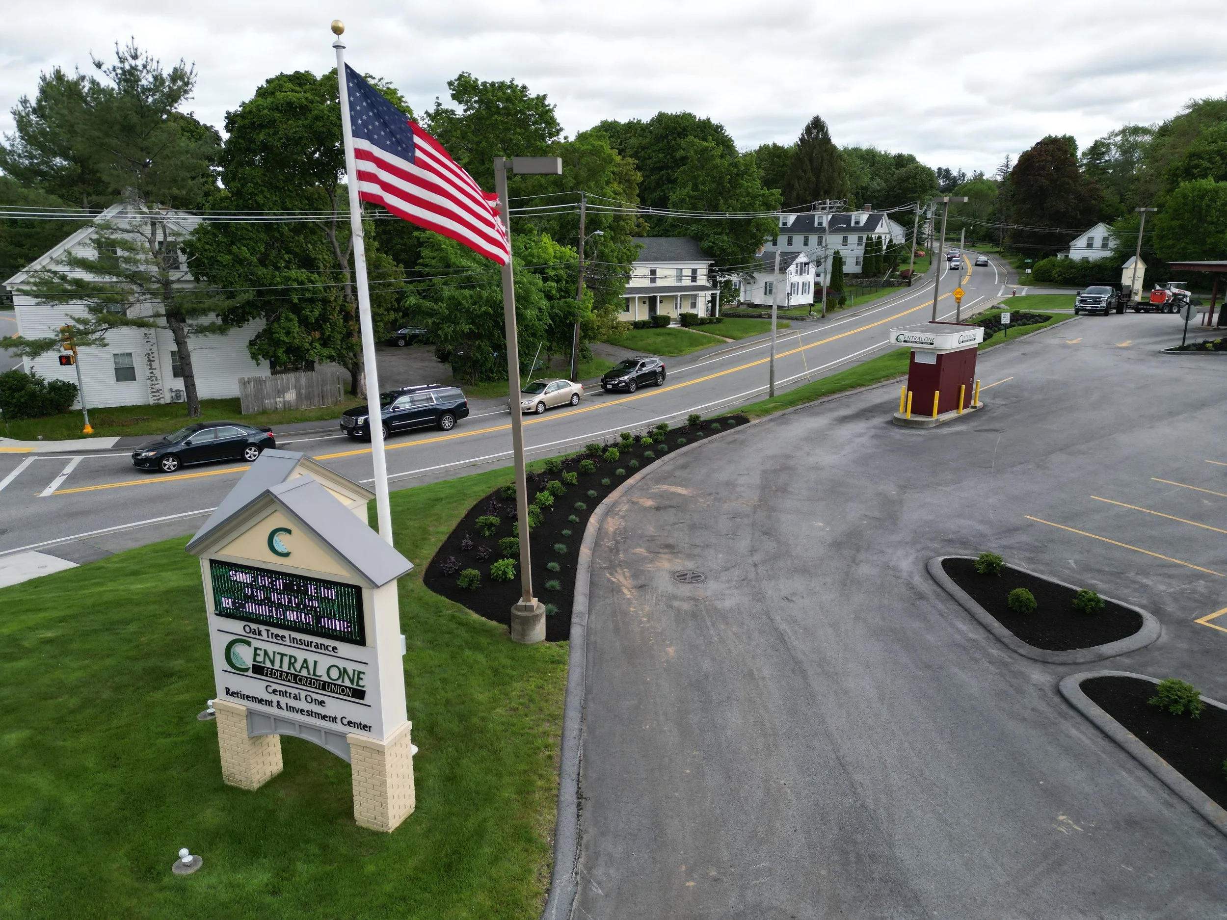 American flag flying outside a Central One Federal Credit Union branch overlooking a tree-lined residential street.