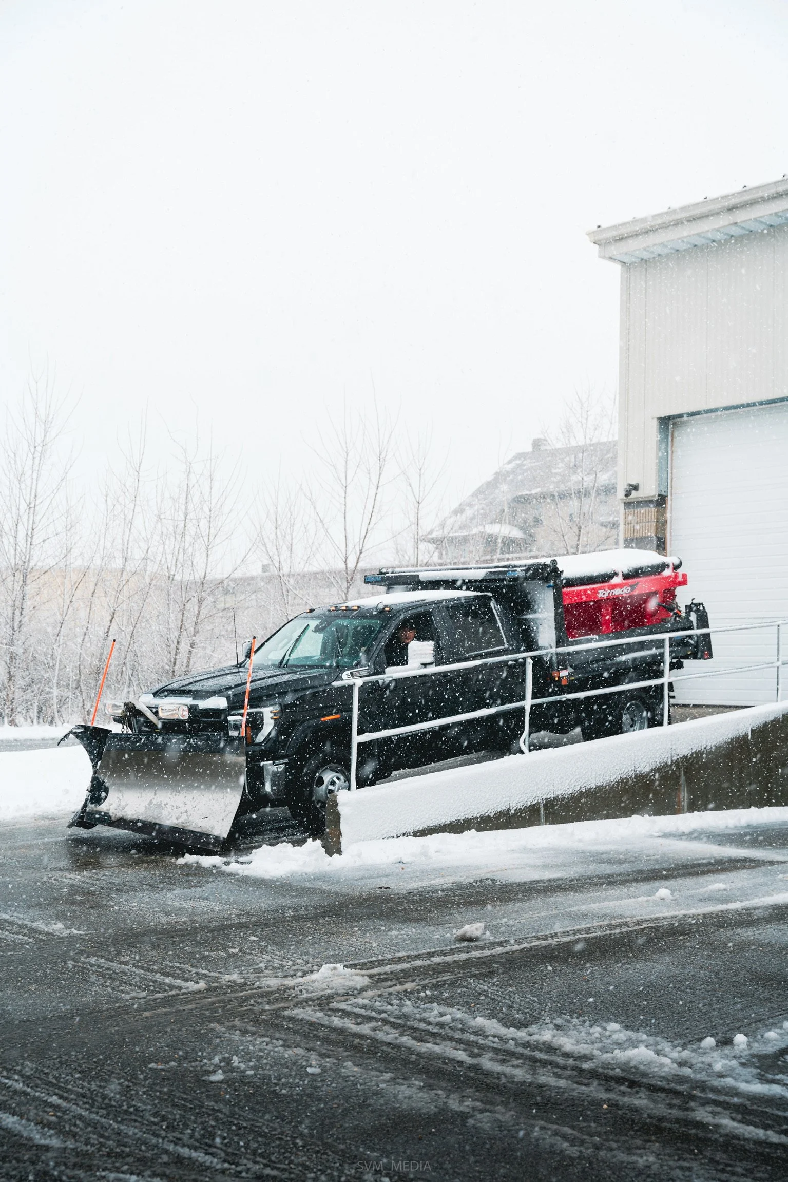 A snow plow truck clearing snow from a driveway during a snowstorm.