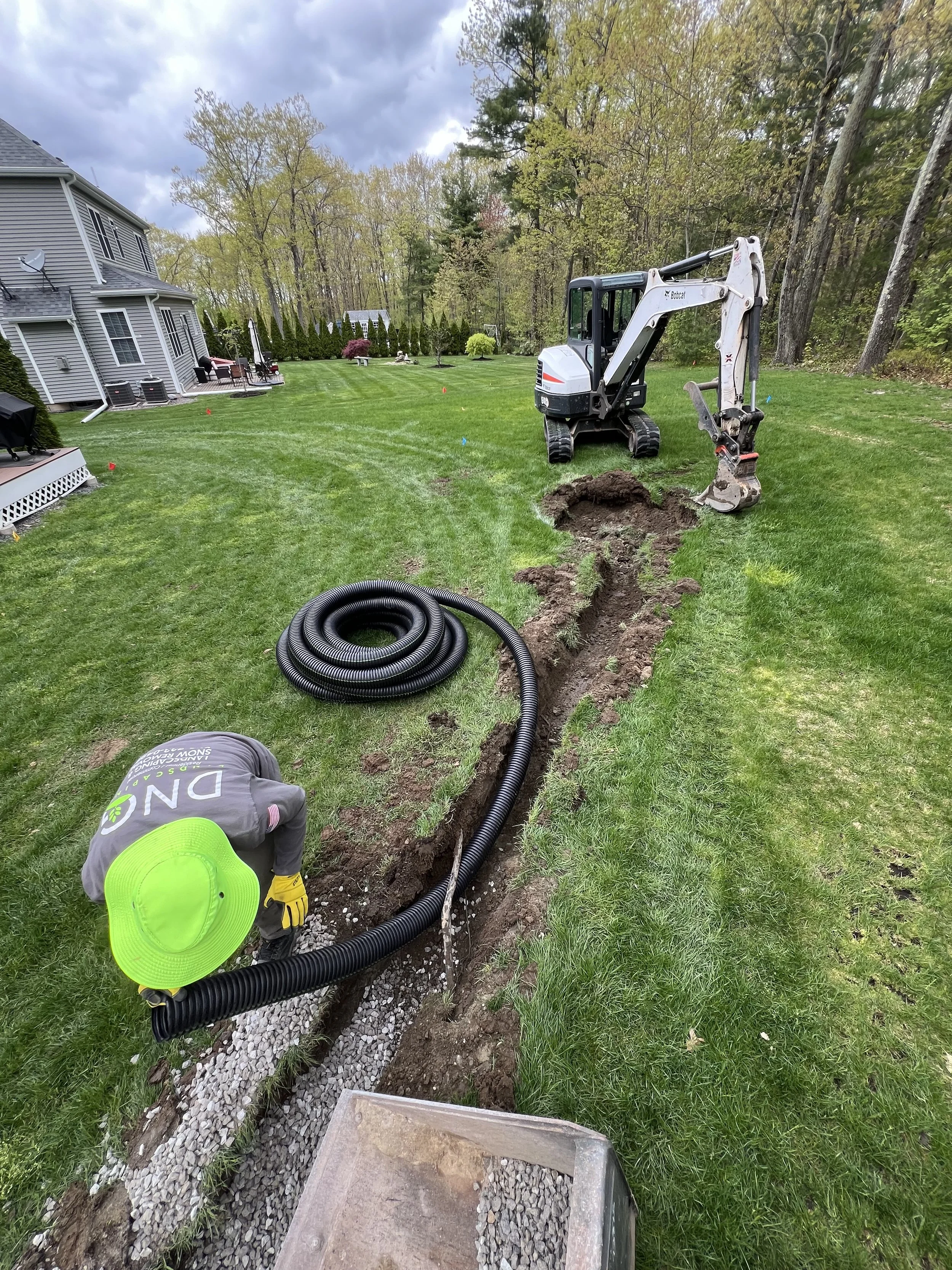 Bobcat mini excavator digging a trench for black drainage pipe in a residential backyard