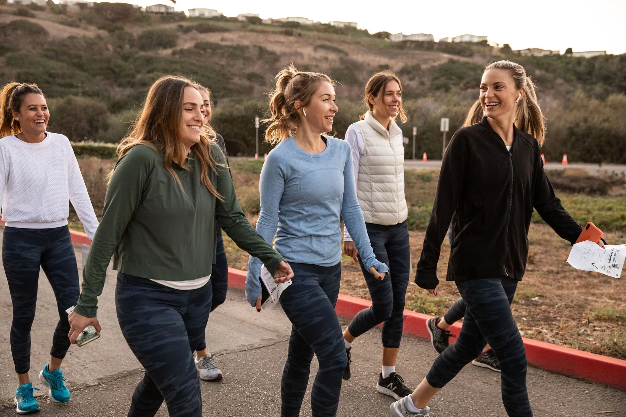Five women in athletic clothing walking together outdoors along a coastal hillside trail.