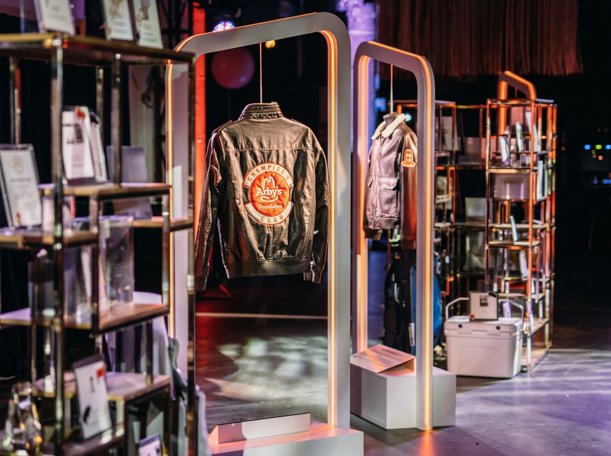 Display of jackets on illuminated racks at an exhibition or store, with shelves and informational plaques nearby.