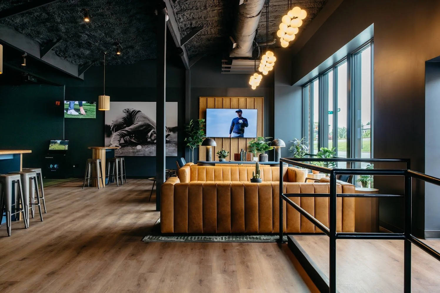 Modern coffee shop interior with leather seating, large windows, wall art, plants, and a television.