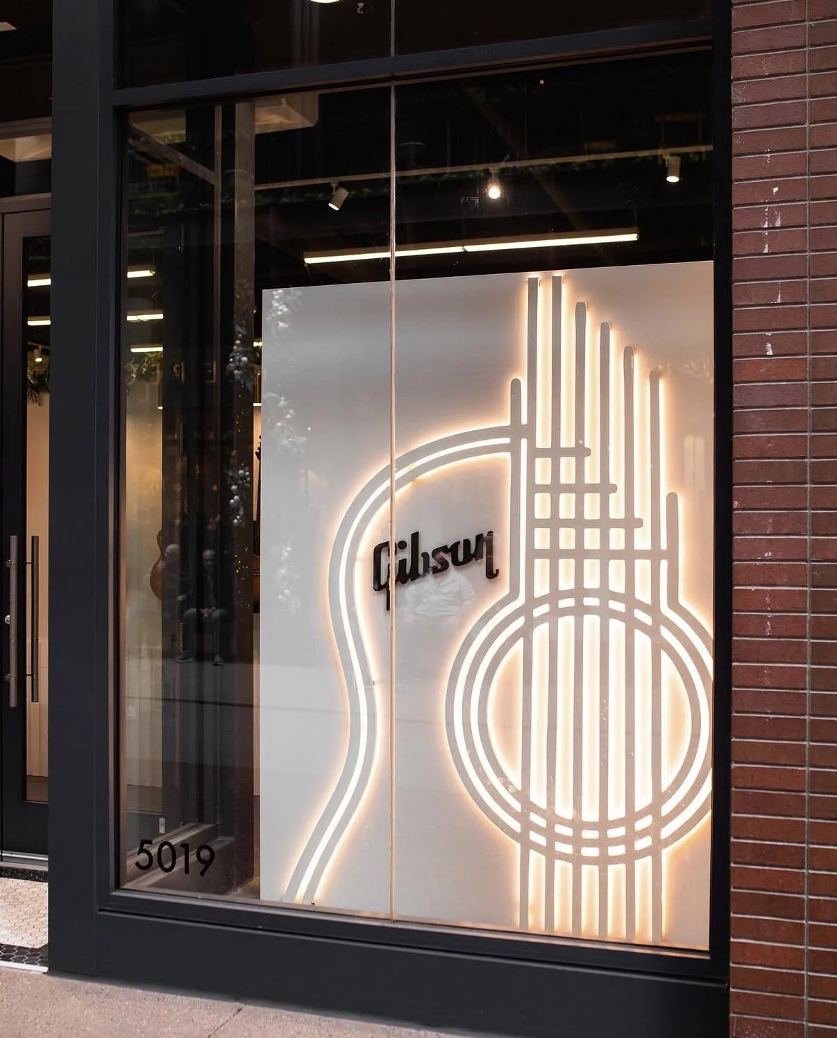 Storefront window with a neon outline of a guitar and the word 'Gibson' inside the guitar shape.