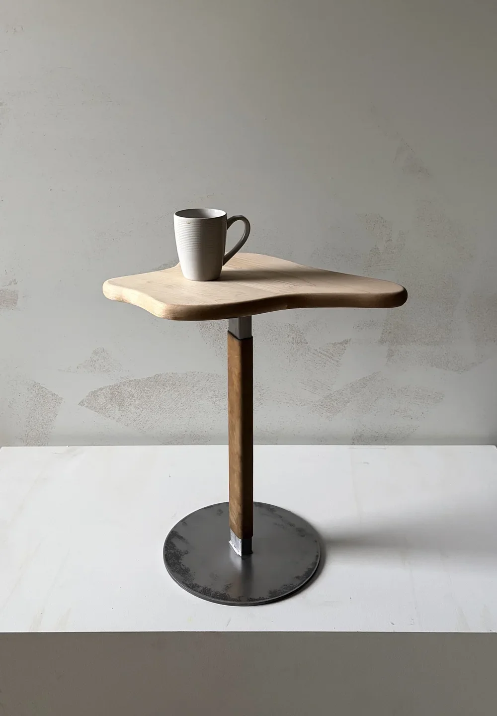 Blank ceramic mug on a minimalist wooden table with a metal base, against a plain background.