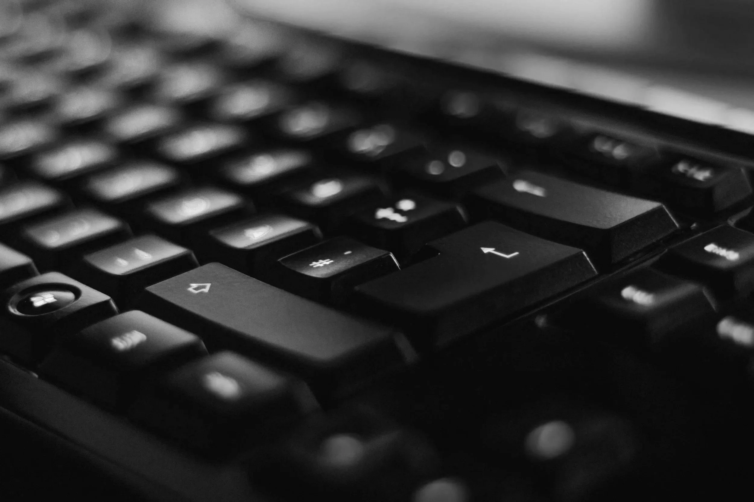 Close-up of a black computer keyboard in black and white, highlighting several keys including arrow keys and number keys.