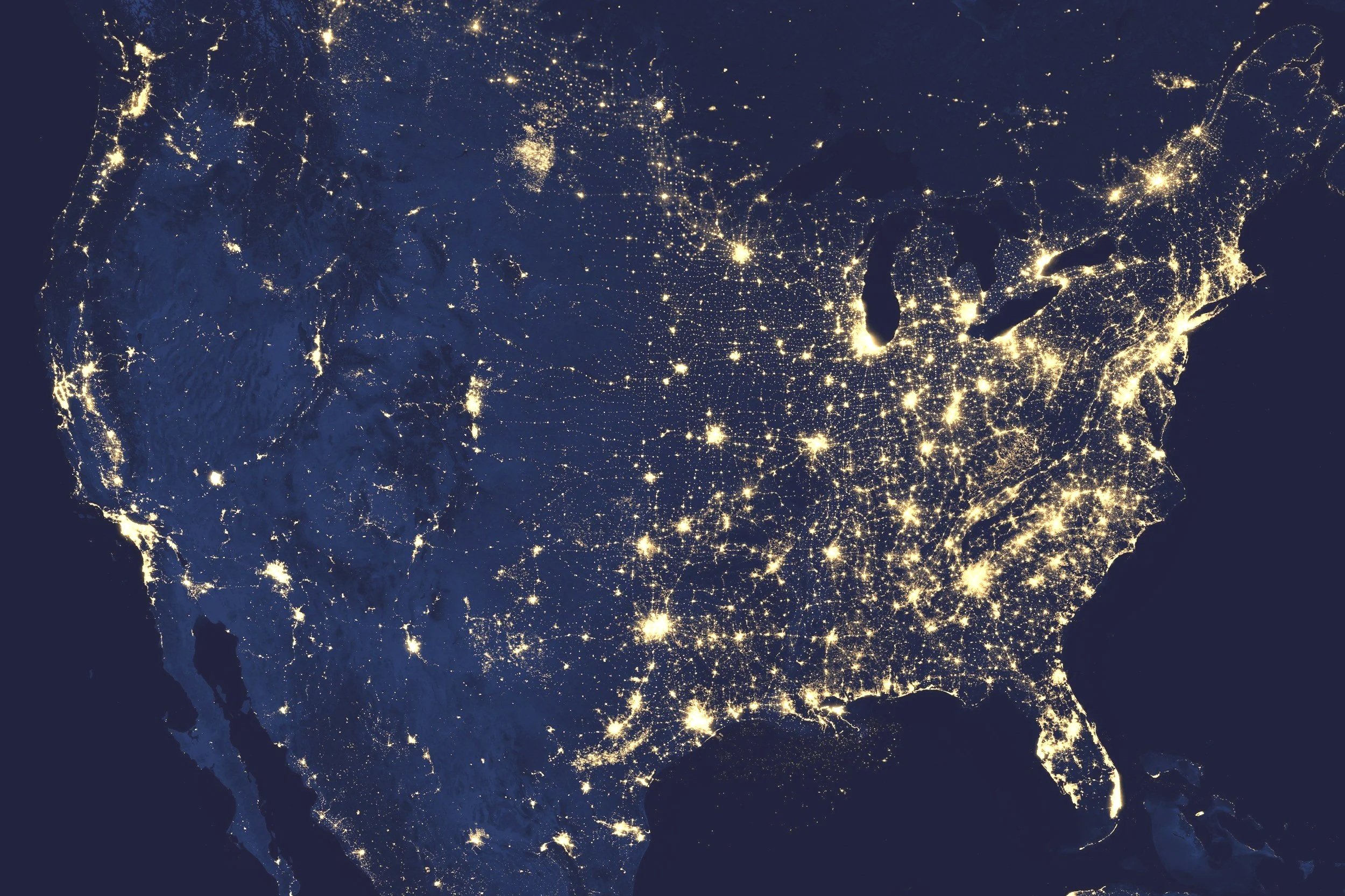 Satellite image of the United States at night showing illuminated cities and urban areas.
