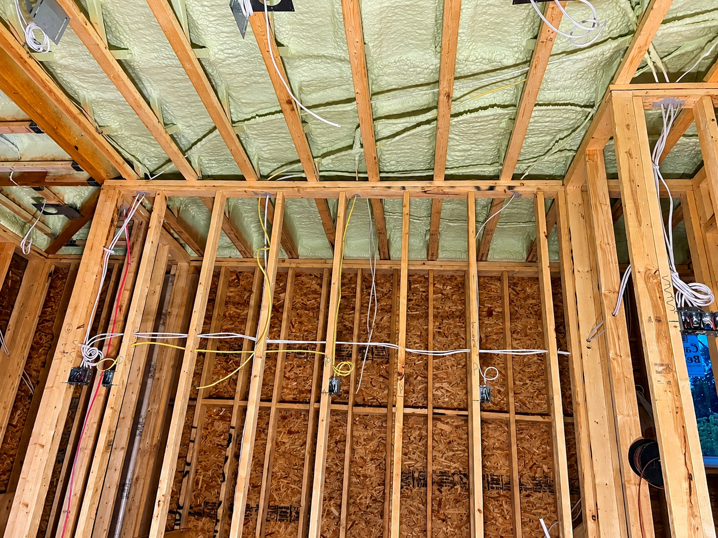 Construction framing with exposed wooden studs, electrical wiring, and insulation on the ceiling and walls.