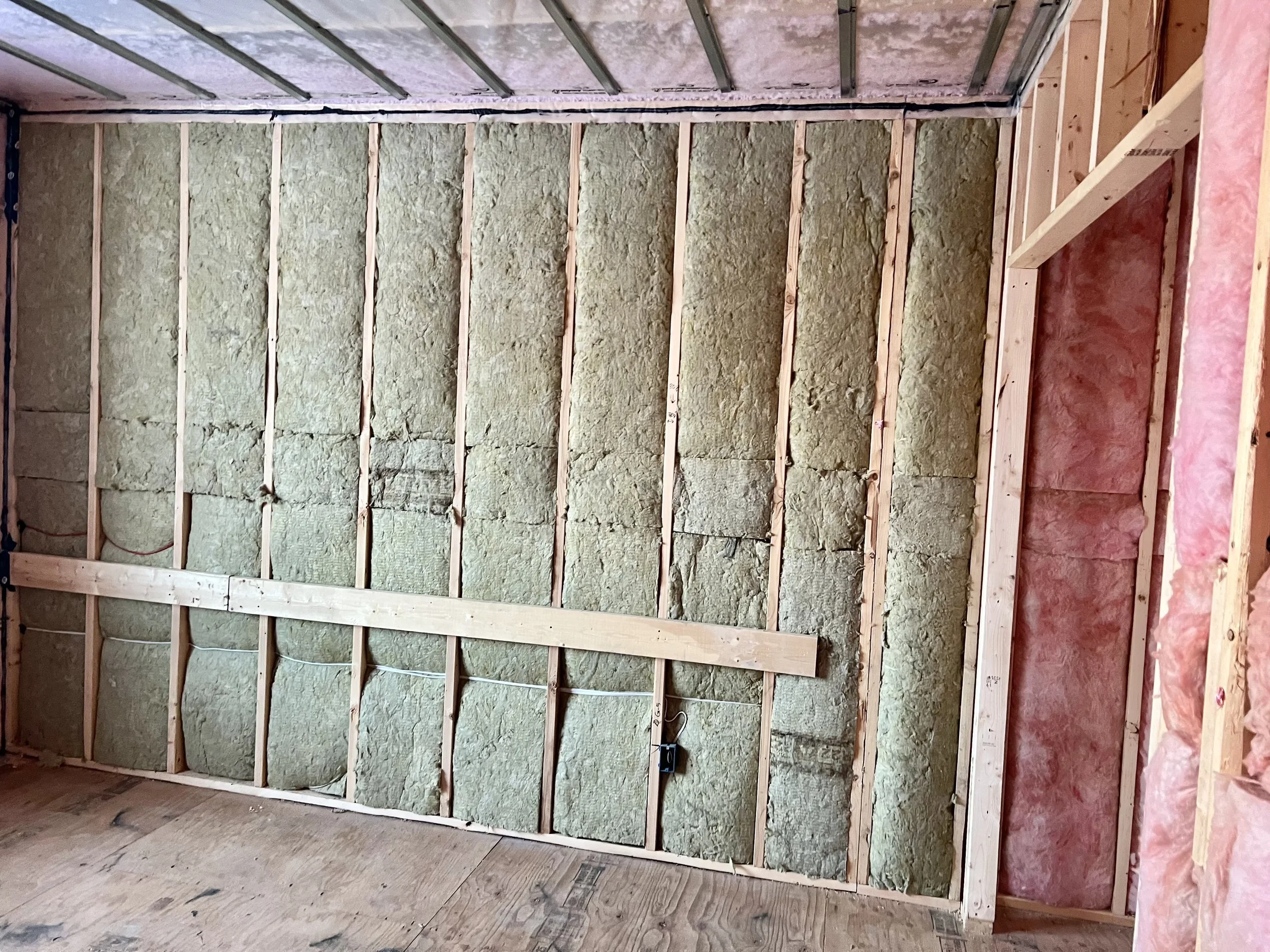 Interior of a house under construction showing wall framing with insulation and pink insulation on the right side.