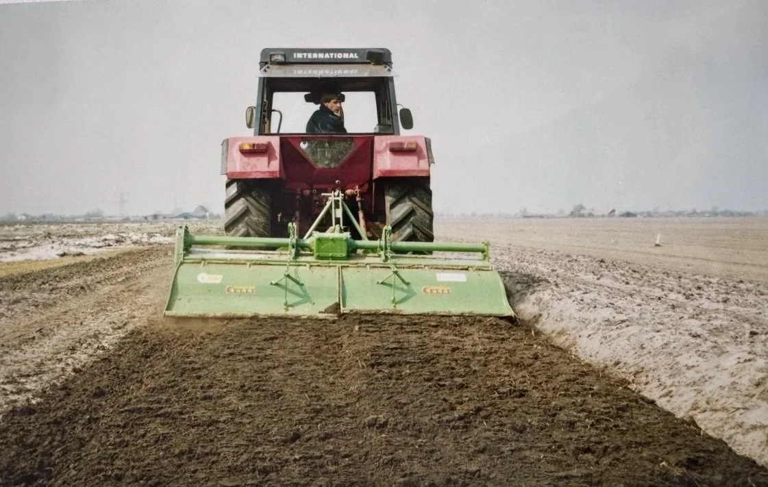 Een tractor ploegt een uitgestrekt veld vroeger toen Huetink is opgericht