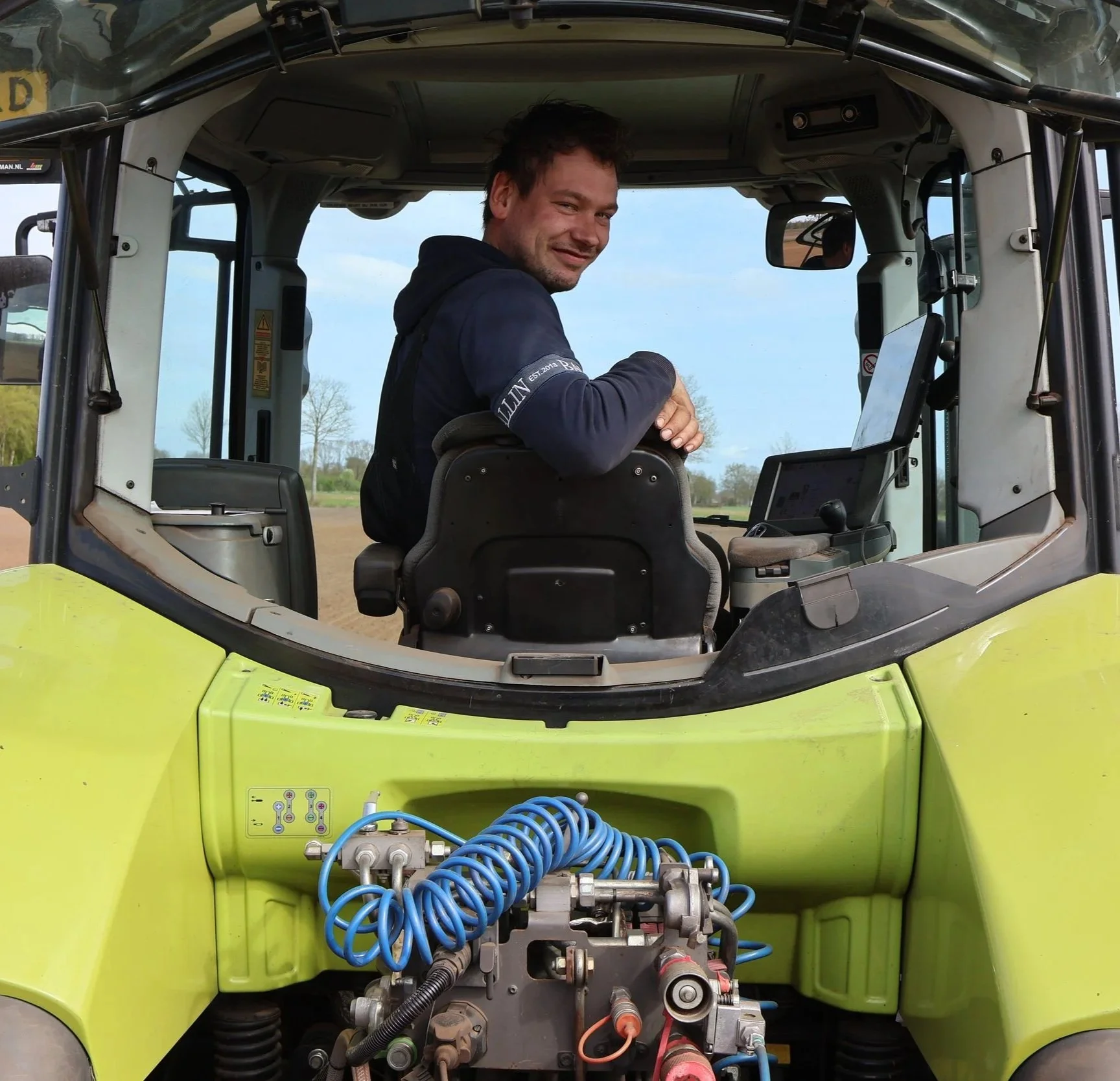 Een man zit in het cabines van een tractor terwijl de motor en technische onderdelen zichtbaar zijn in de voorkant.