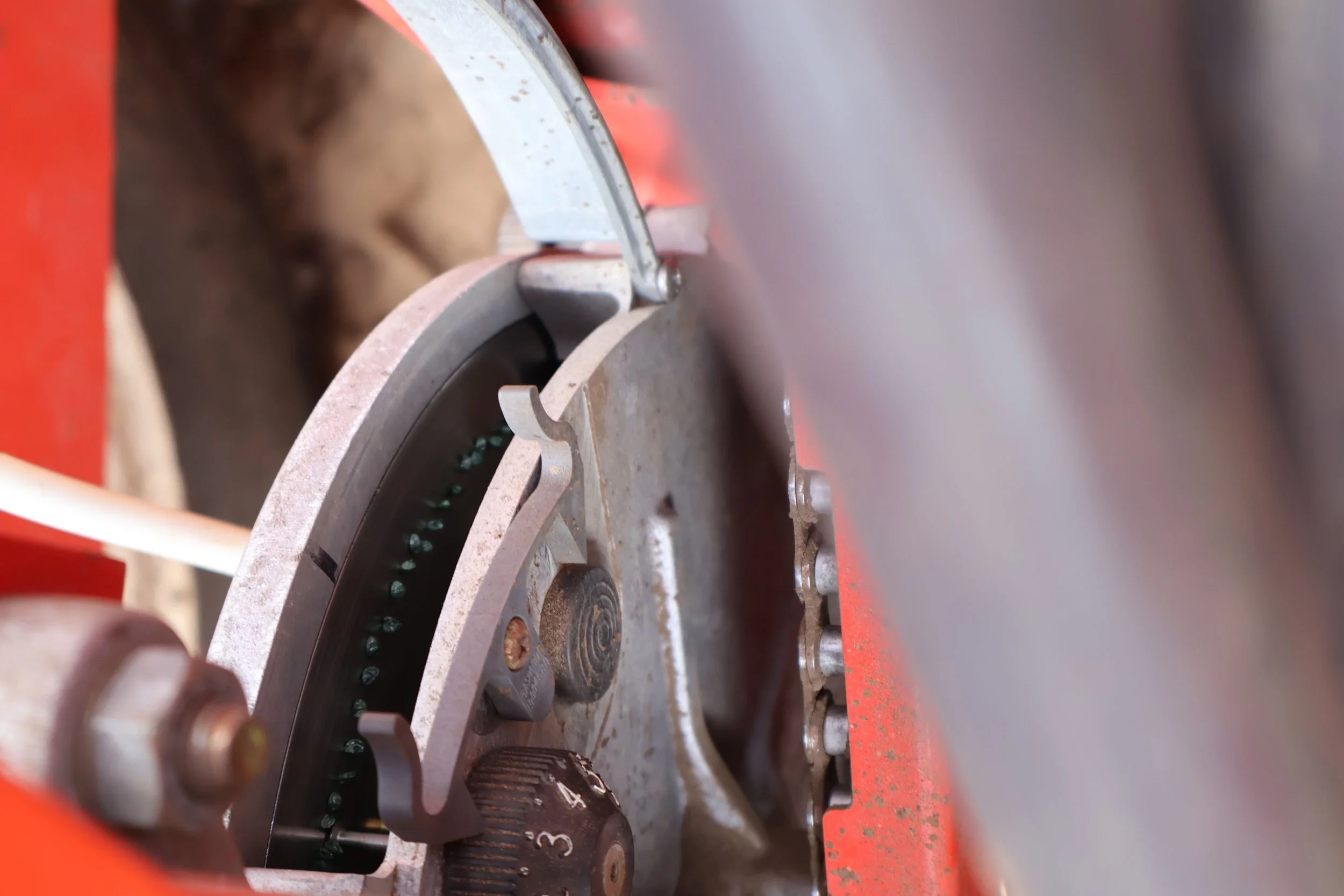 Close-up van een metalen onderdeel van een machine met tandwielen, schroeven en een slijpmachine op een rode basis.