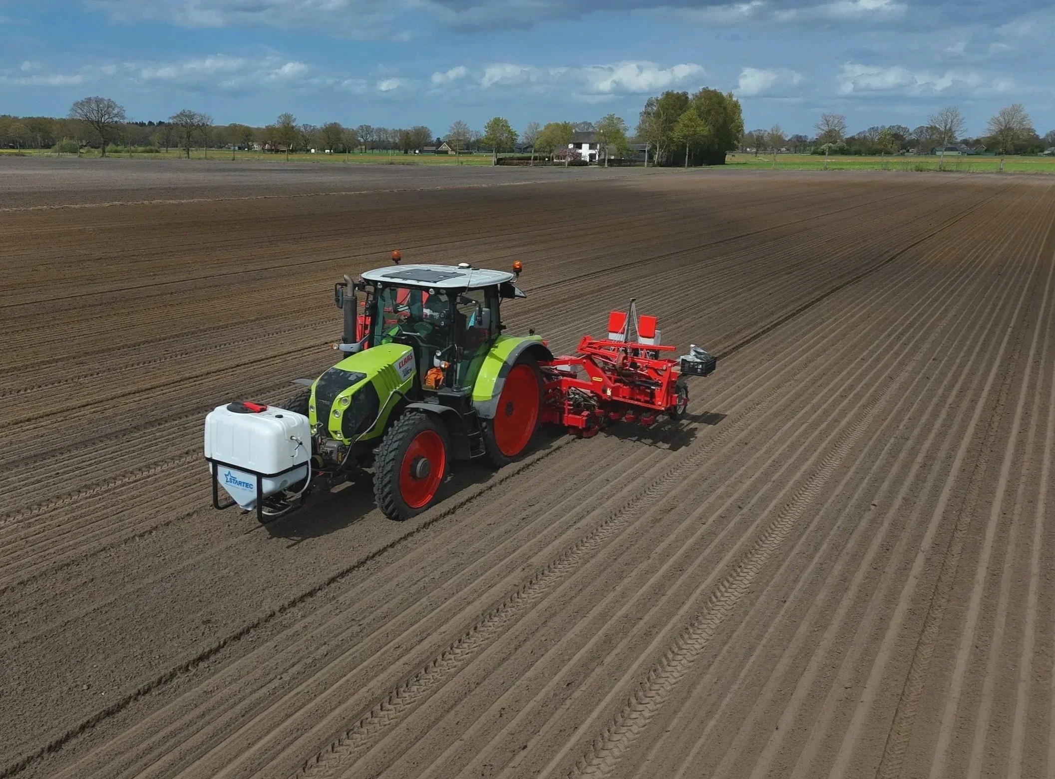 Een tractor die de grond bewerkt op een landbouwveld onder een deels bewolkte hemel.