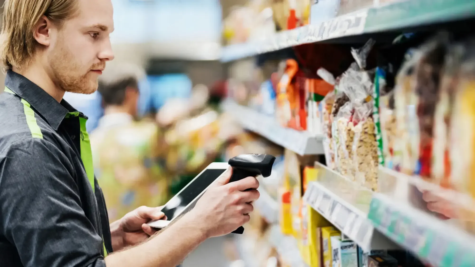 A man shopping in a grocery store using a handheld barcode scanner to scan merchandise on the shelf.