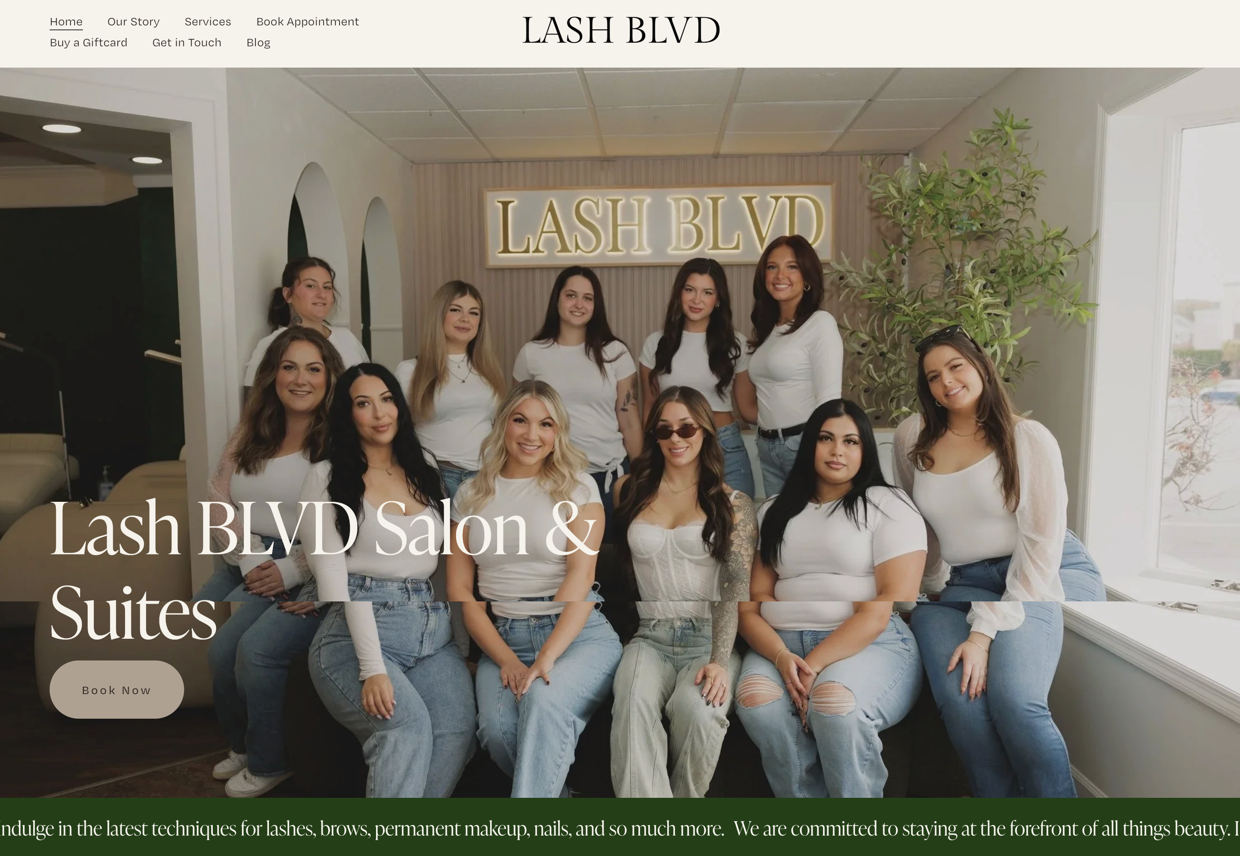Photo of a group of women sitting and standing together inside a beauty salon called Lash Blvd, with a sign behind them that reads Lash Blvd. The women are smiling and dressed casually in white tops and jeans.