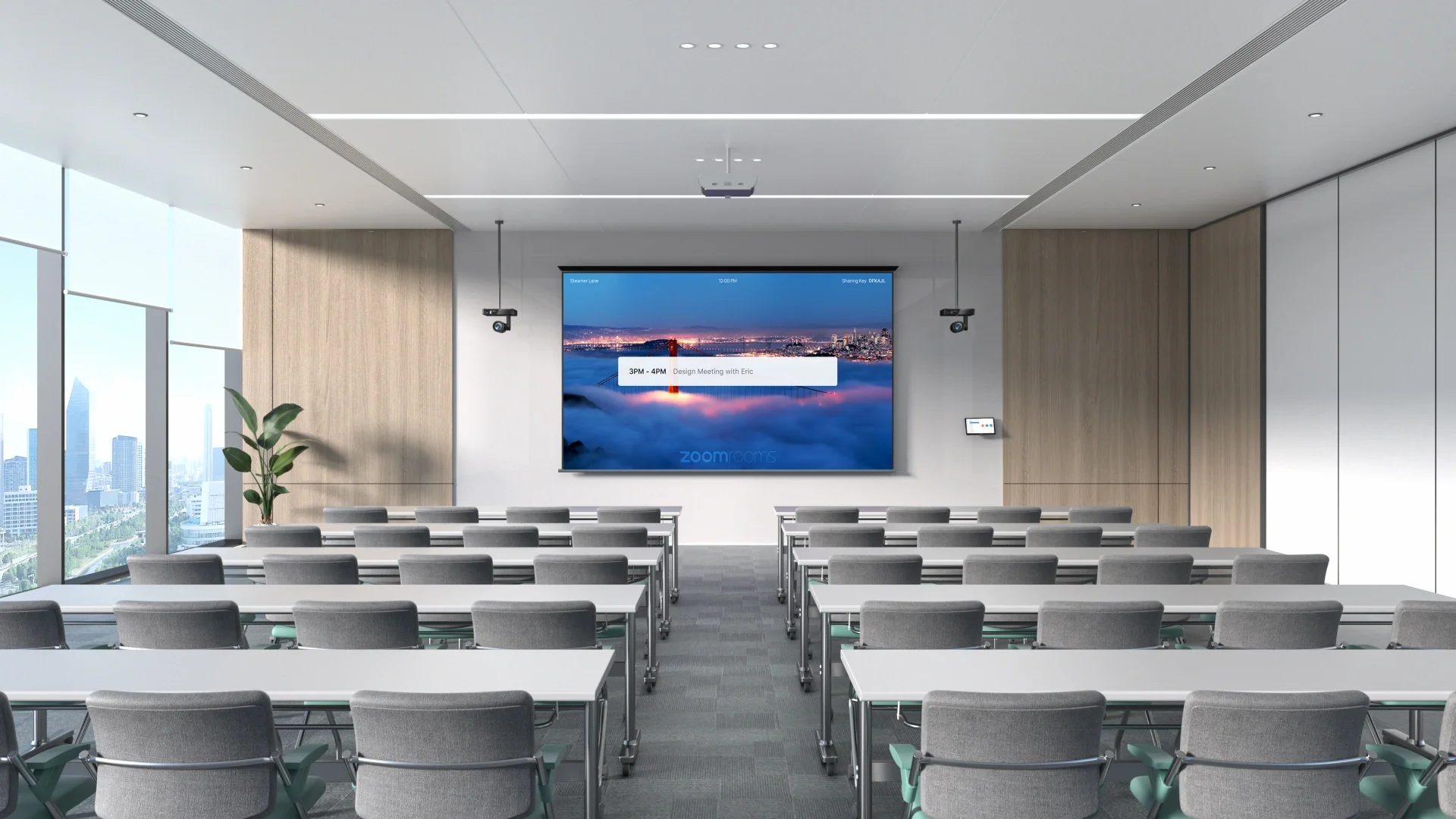 A modern conference room with multiple gray chairs and white tables arranged in rows, a large digital screen displaying a cityscape with the text '3PM - 4PM Design Meeting with Eric,' two ceiling-mounted projectors, two wall-mounted speakers, large windows on the left side revealing a city skyline, and a small control panel on the right wall.