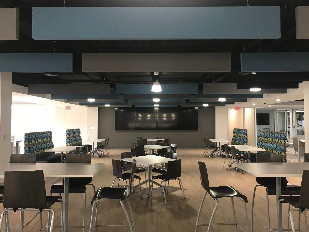 Empty modern cafeteria with white tables, black chairs, and a large black screen on the back wall.