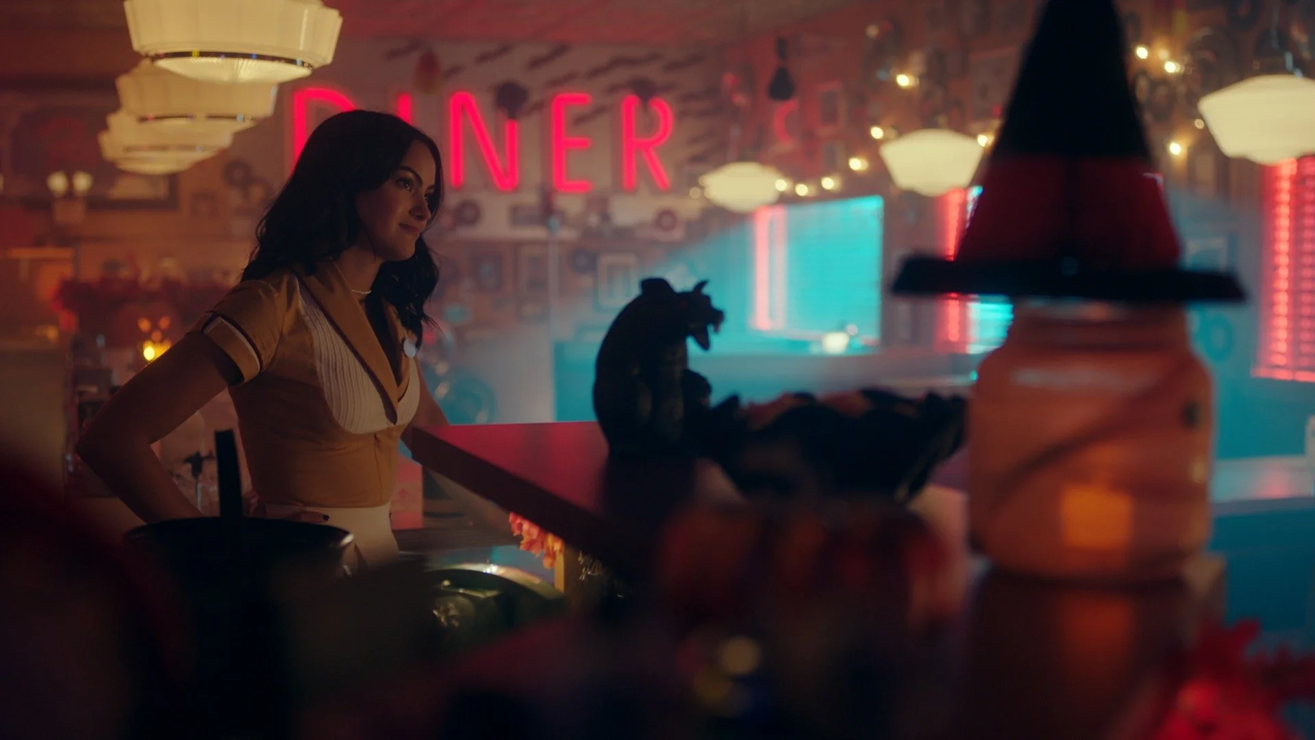 Still from Riverdale, featuring a woman with dark hair in a retro diner illuminated by pink and blue neon lights, shot by director of photography Shamus Whiting-Hewlett.