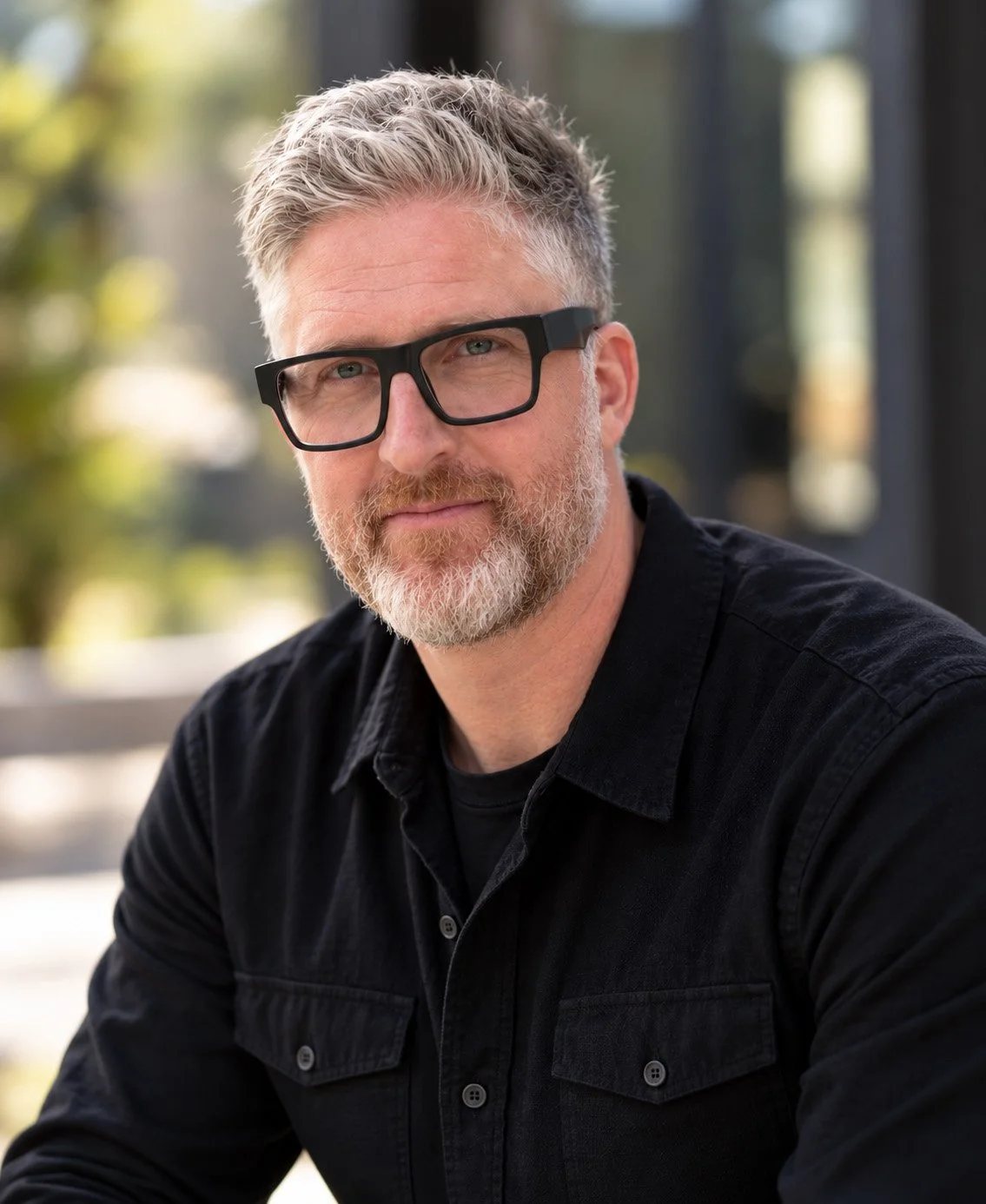 Portrait of Shamus Whiting-Hewlett, Director of Photography, wearing a black shirt and glasses outdoors.