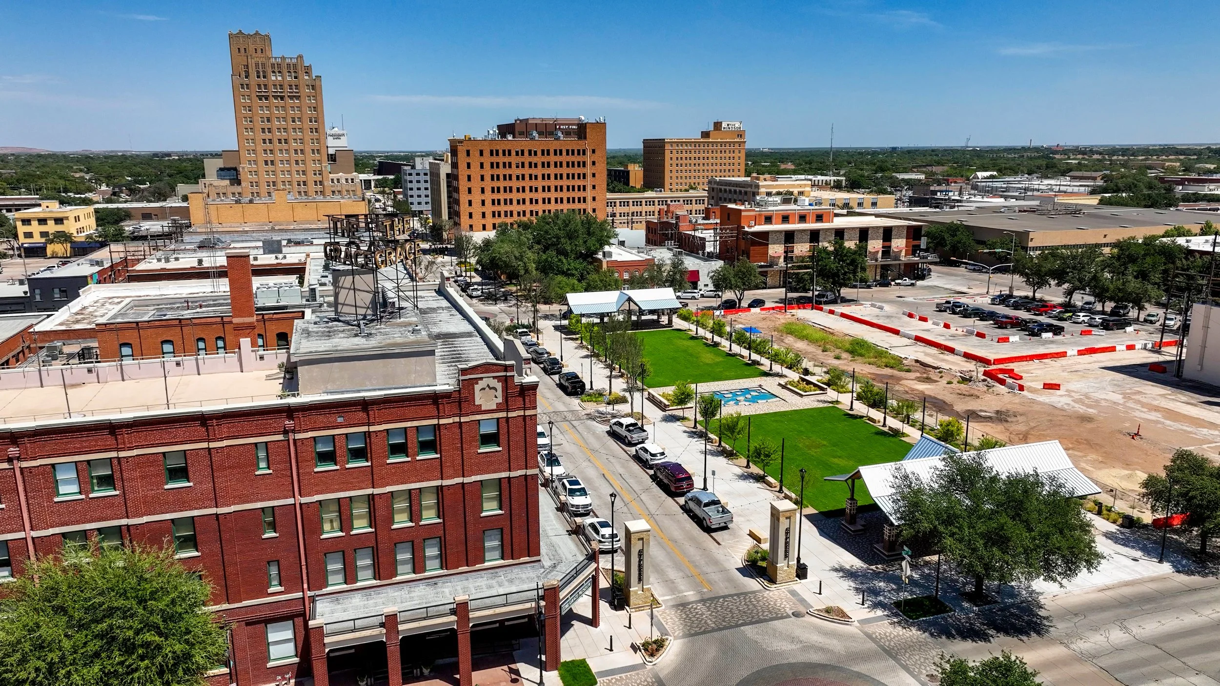 Aerial view of downtown Abilene, Texas, featuring the historic Grace Museum, a landscaped park, streets, and construction activity under a clear blue sky.