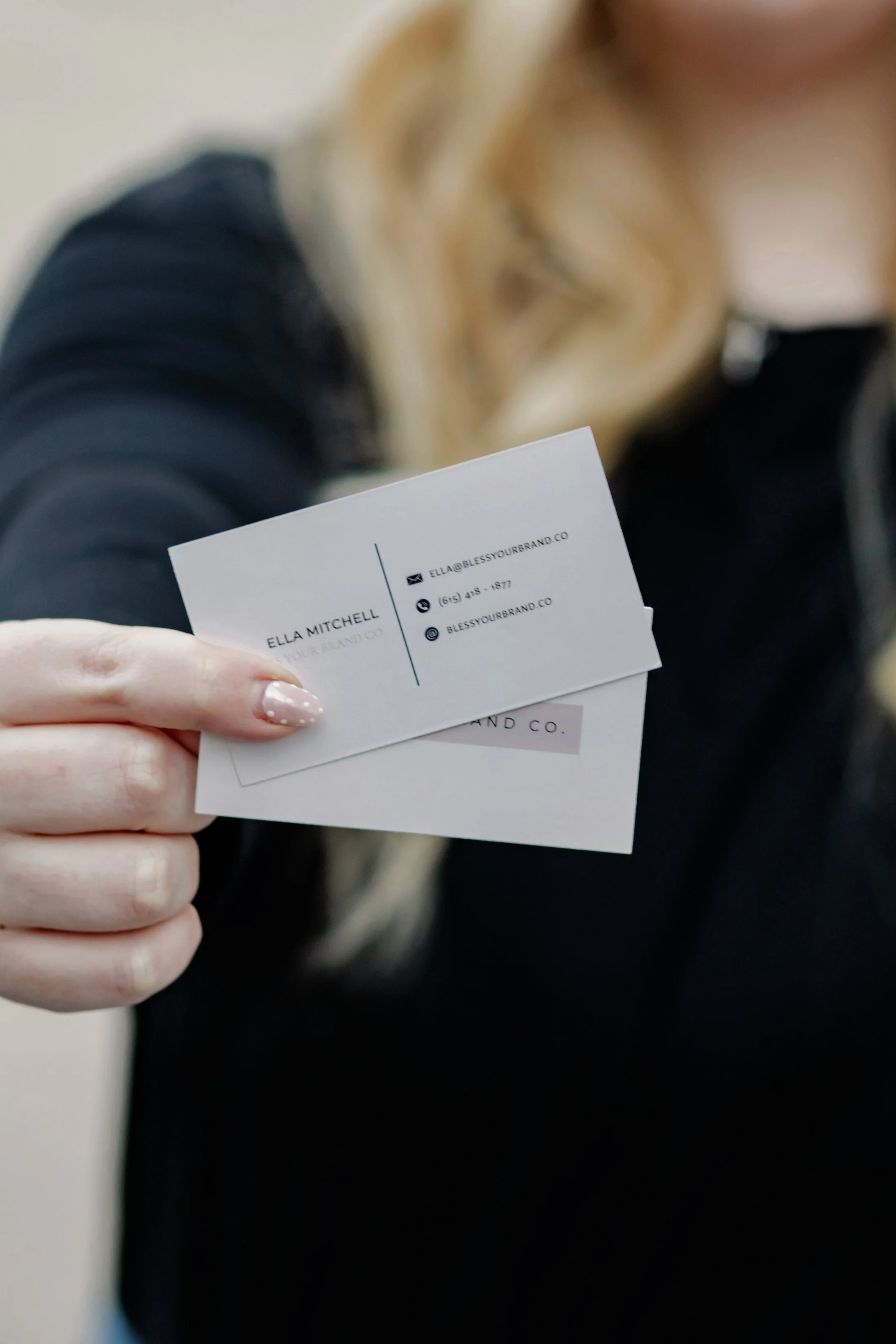 Close-up of a woman holding a business card with contact information, with blurred face and background.