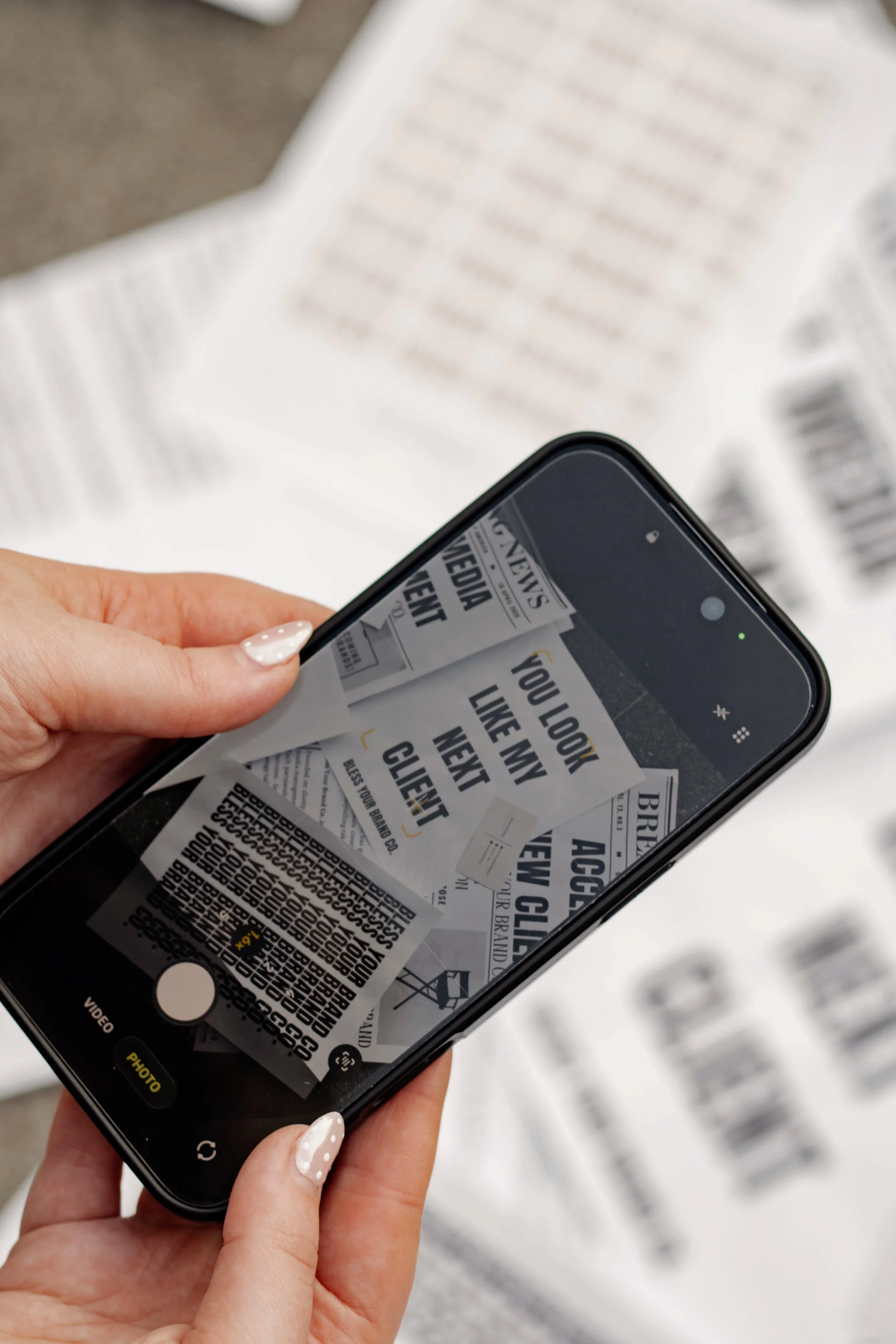 A person holds a smartphone scanning a printed receipt with multiple black and white coupons, with some text visible on the receipt.