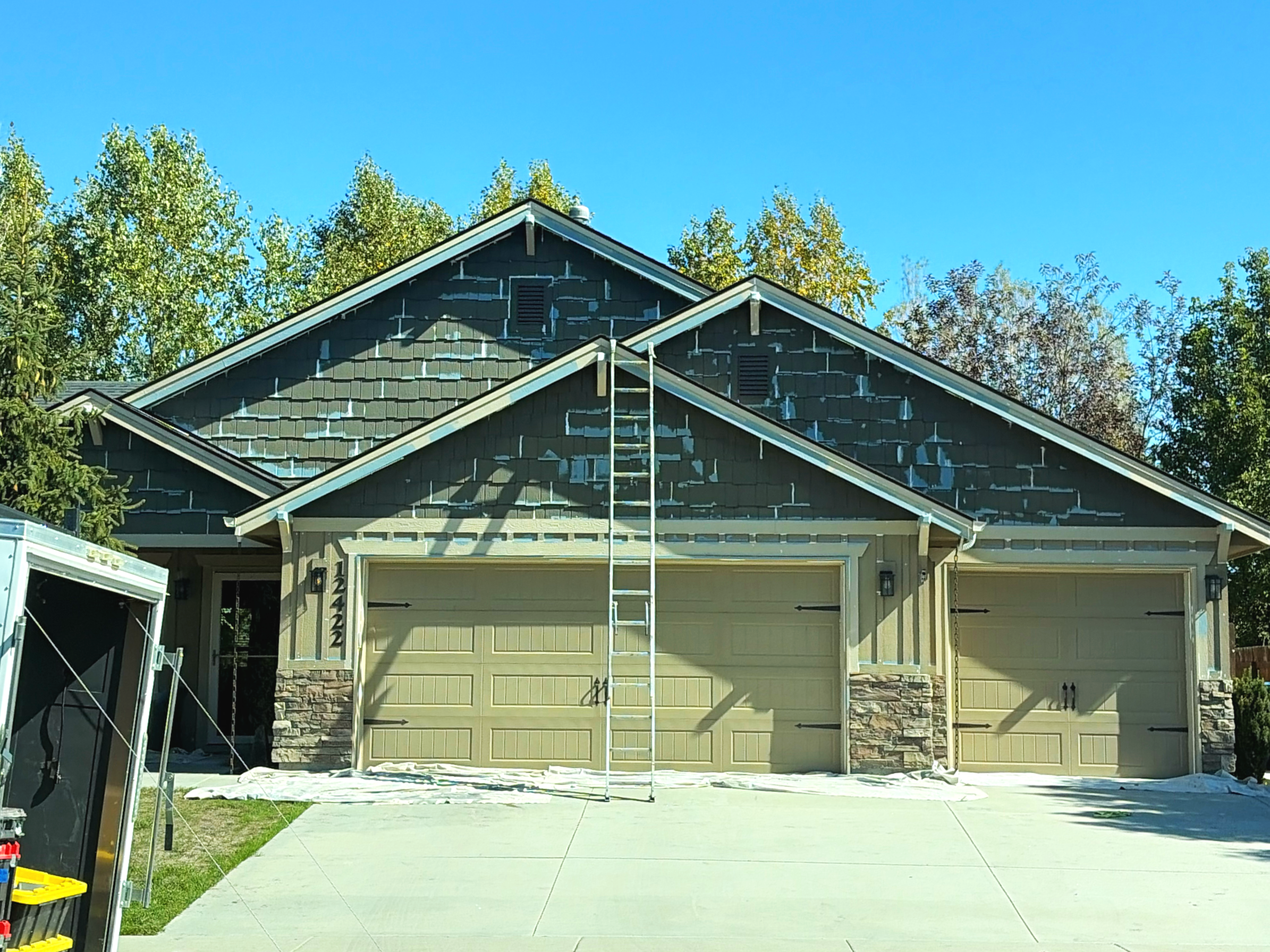 Front view of a house under renovation with a ladder leaning against the roof, exterior painting in progress