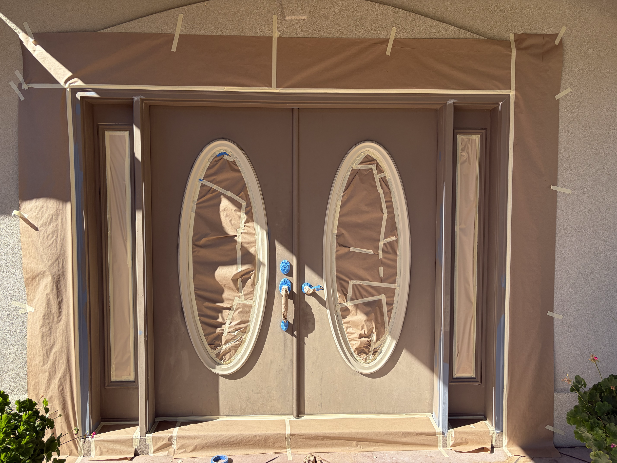 Front door with masking tape outlining window frames, brown paper covering windows, and blue painter's tape on some areas of the door, indicating preparation for exterior painting in Meridian, Idaho