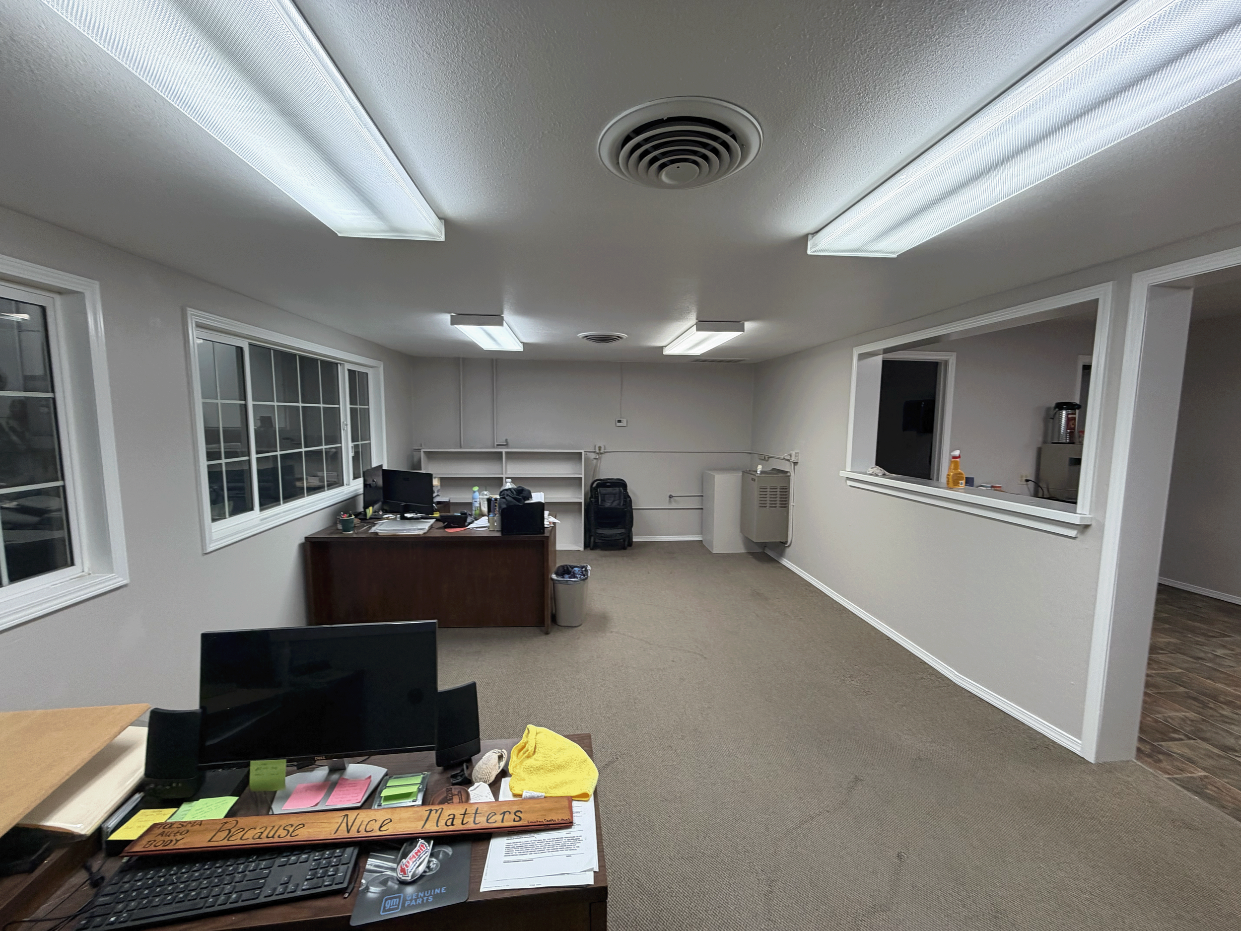 Office space with white walls, ceiling vents, fluorescent lighting, a window, and a desk with a computer, papers, a yellow towel, and office supplies. Commercial interior painting in Meridian, Idaho