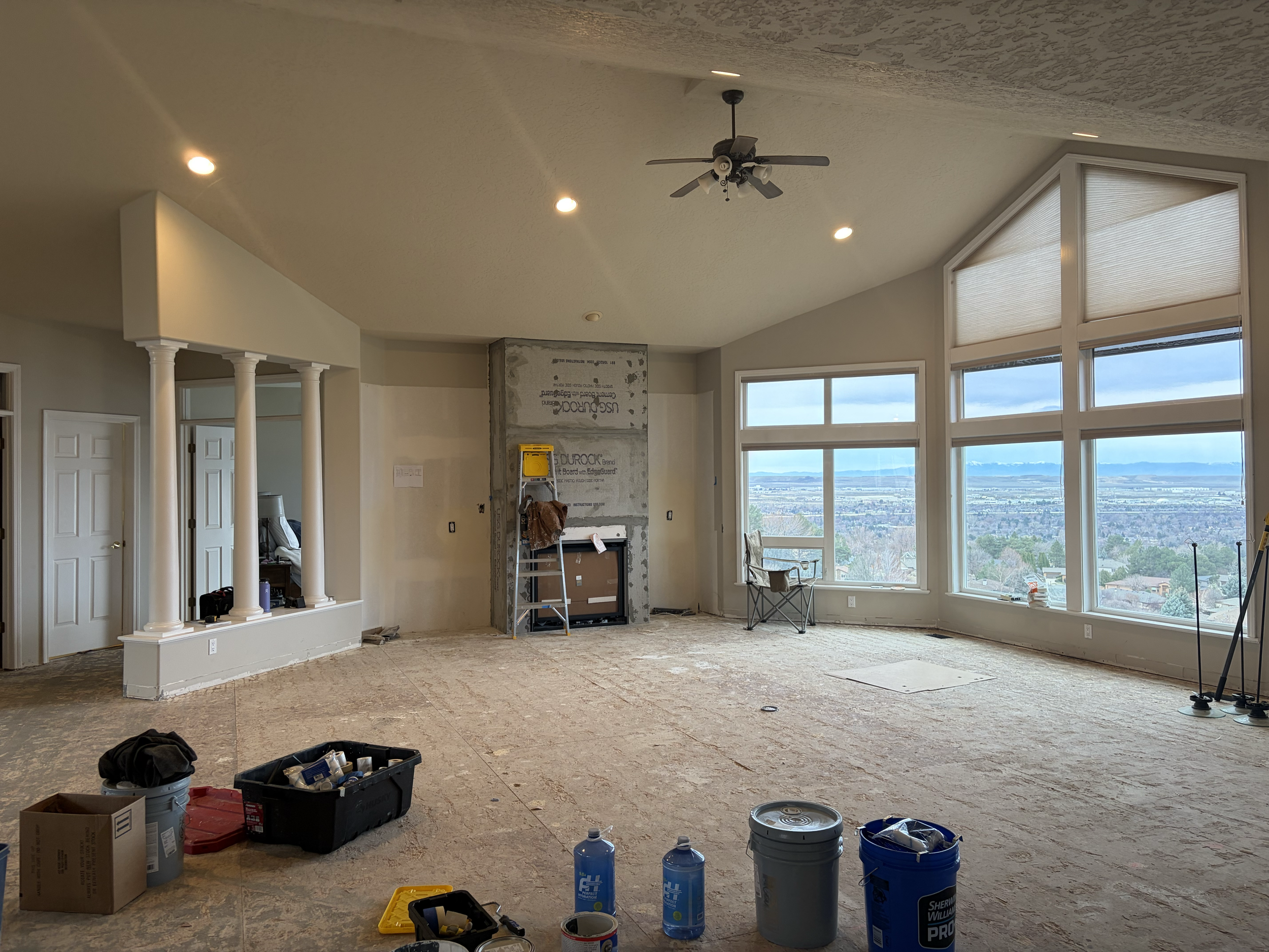Interior of a room under construction with large windows, construction tools, bottles, and building materials on the floor, and ceiling lights. Luxury home interior painting in Boise, Idaho