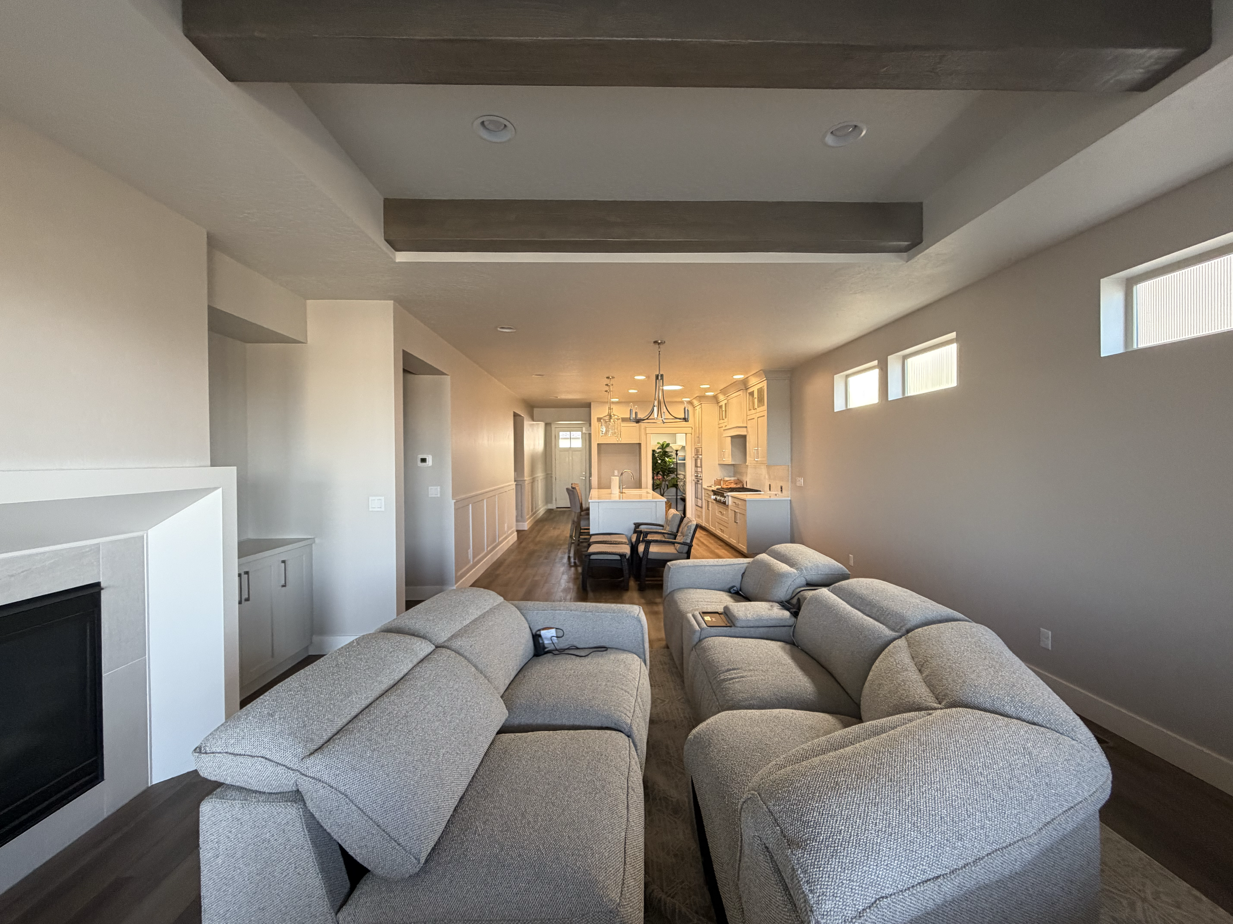 Living room with gray sectional sofa, beige walls, dark wood floor, and a high ceiling with wood beams. Windows along one wall let in natural light to showcase the residential interior painting project.