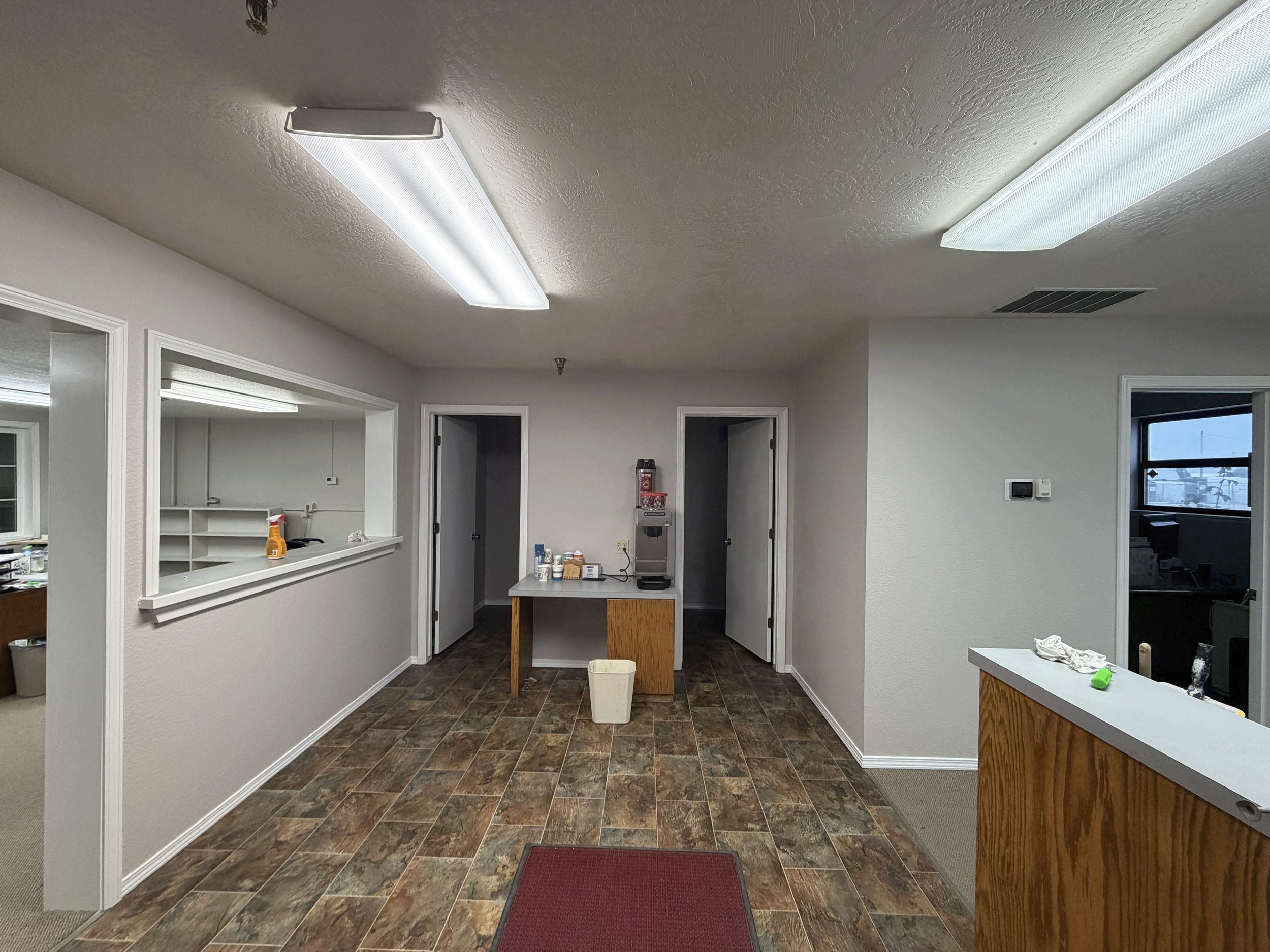 Interior view of a room with a dropped ceiling, fluorescent lights, windows, a water fountain, and a table with cleaning supplies on it. Commercial office painting in Treasure Valley, Idaho