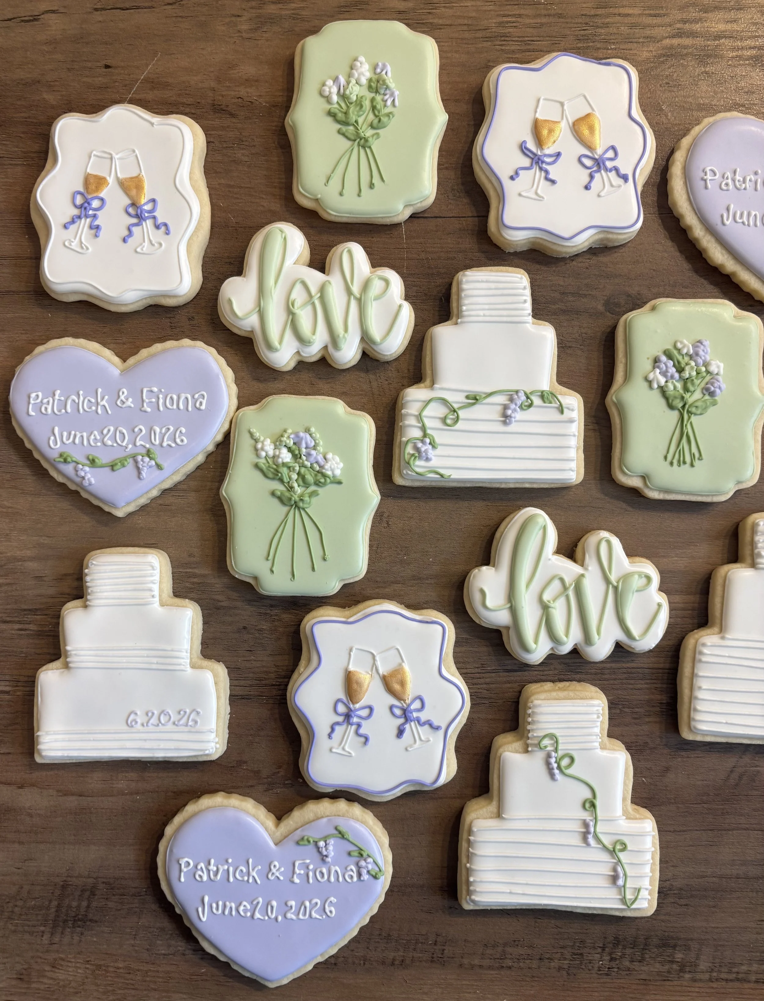 Decorated cookies with wedding and anniversary themes, including champagne glasses, flowers, and personalized messages, displayed on a wooden surface.