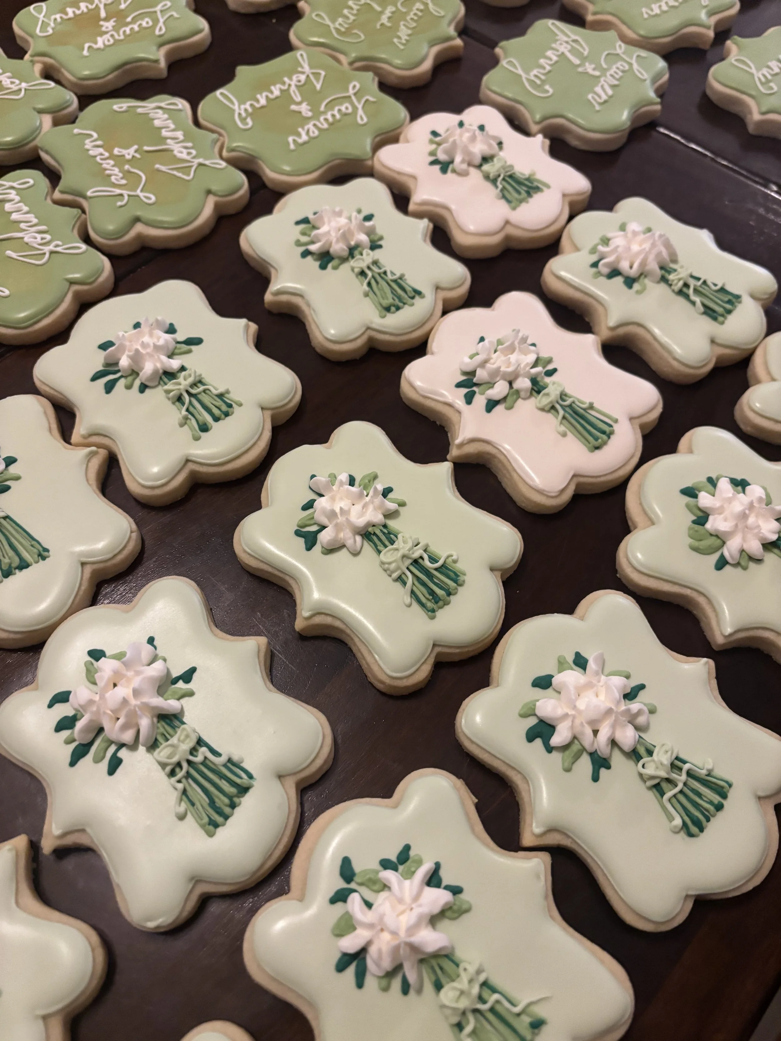 Decorated cookies shaped like flowers with white icing and a bouquet design, arranged on a dark surface.