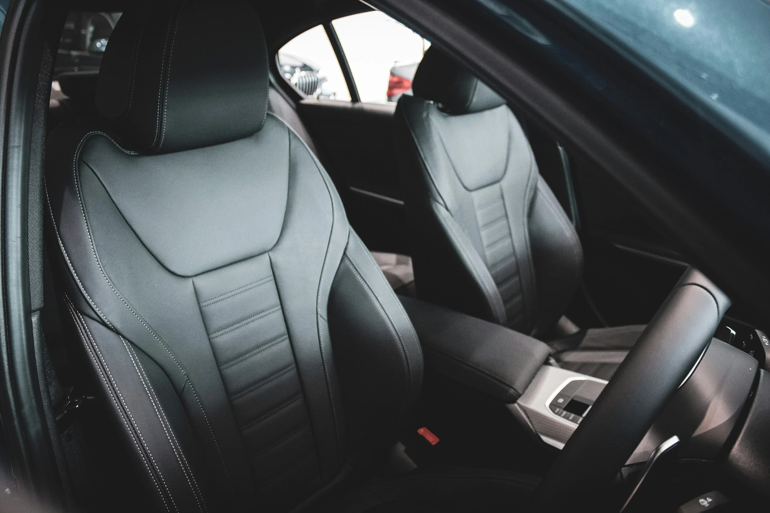 Interior of a modern car showing gray leather seats with white stitching, front seat backs, and center console.
