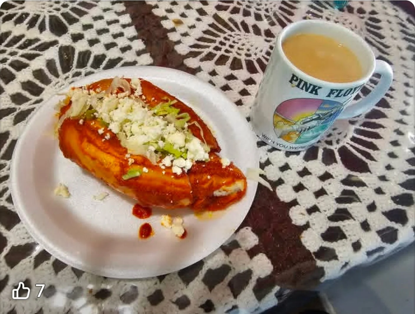 A plate with Mexican food, possibly enchiladas topped with cheese and lettuce served with a cup of hot beverage, on a lace tablecloth.