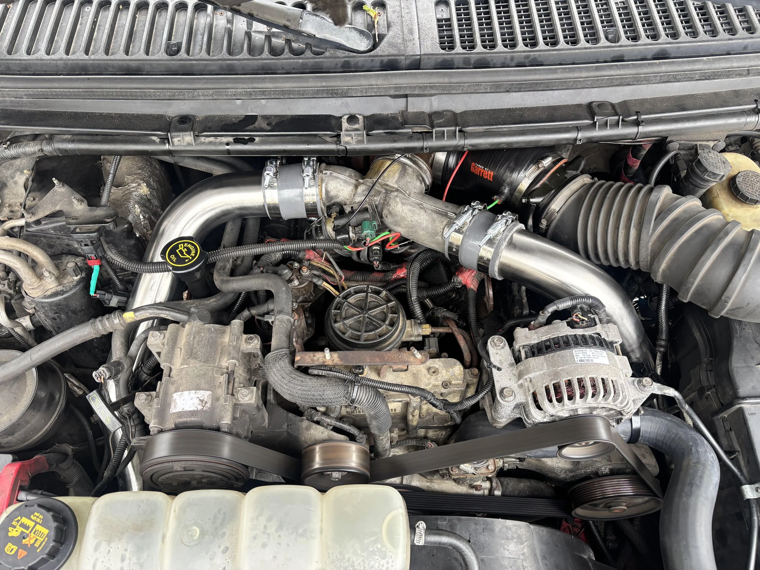 A view of a car engine bay showing various components including hoses, belts, and the air intake system.