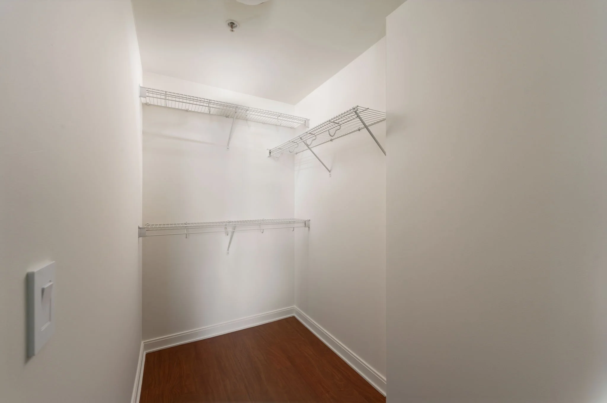 Empty walk-in closet with white wire shelves on white walls and hardwood floor.