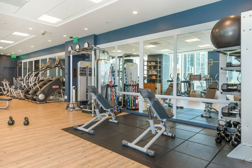 Empty gym with cardio machines, weight training equipment, and a large mirror on the wall.