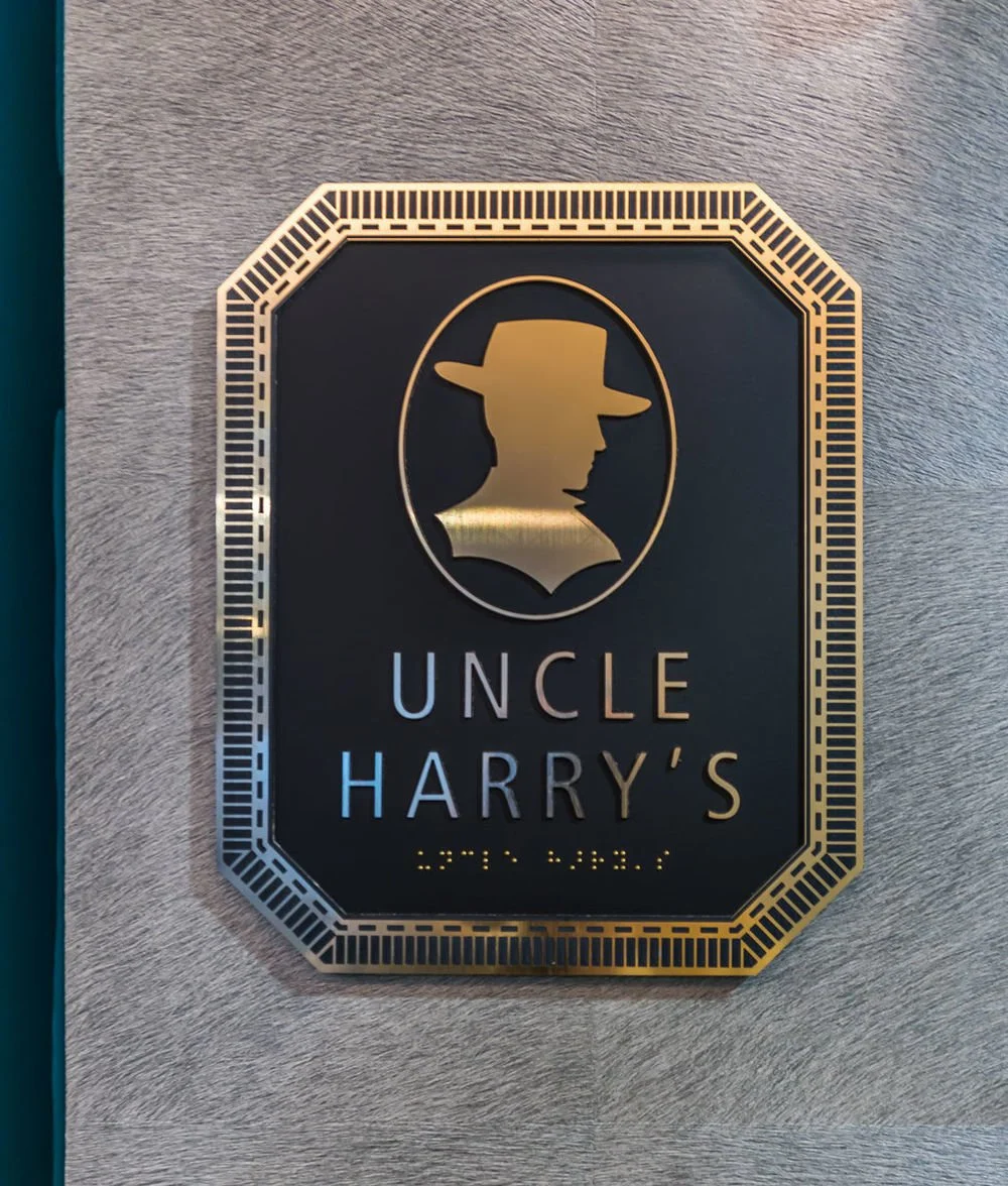 A decorative sign with a silhouette of a man wearing a hat, marked "Uncle Harry's" on a gray textured wall.