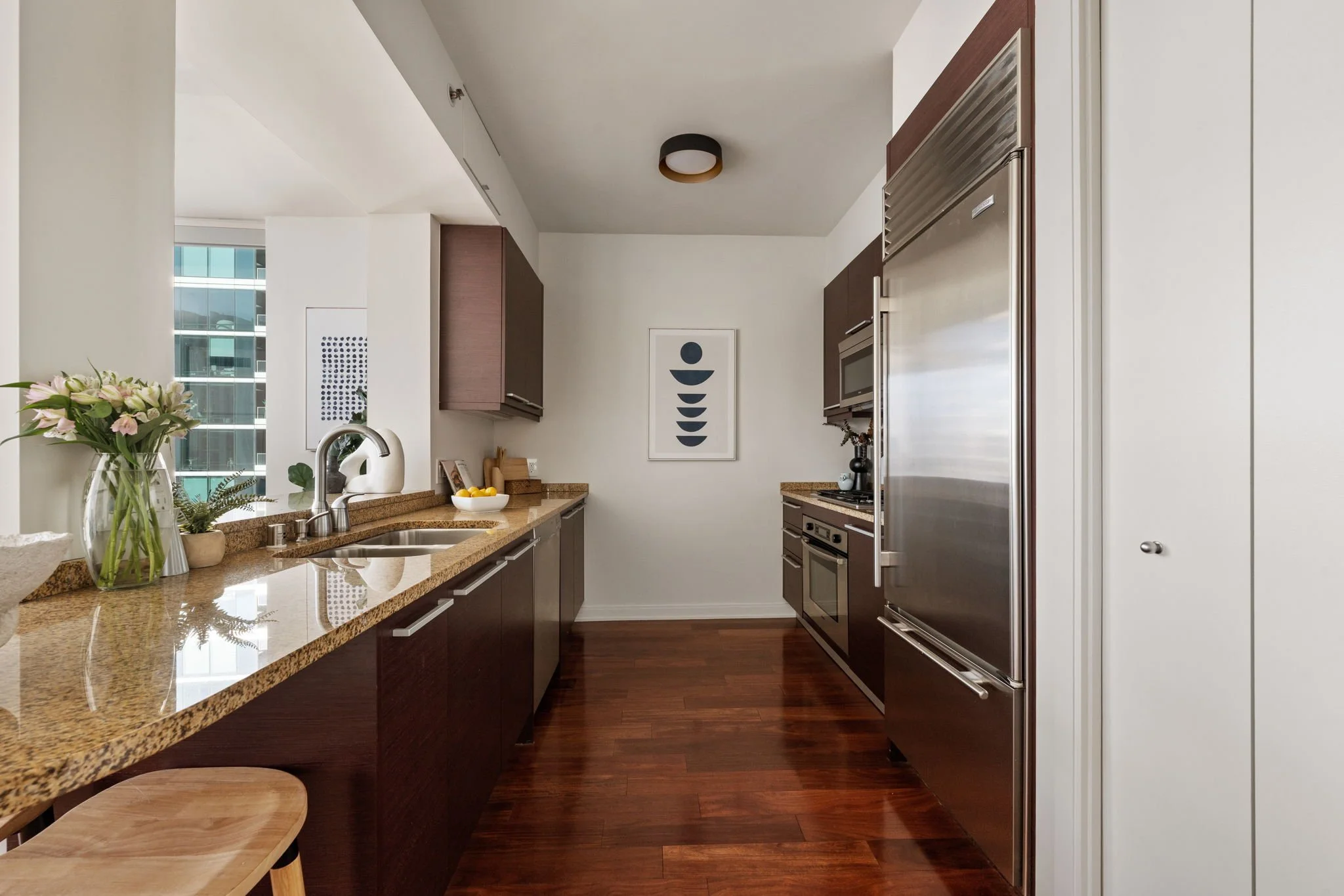 Modern kitchen with dark brown cabinets, granite countertops, stainless steel appliances, a bouquet of flowers, and a framed abstract art piece on the wall.
