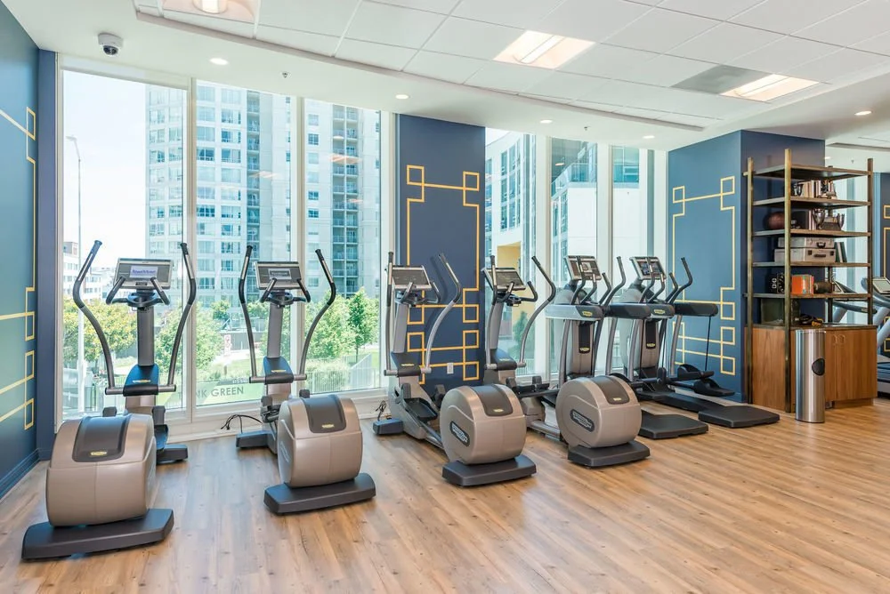 Fitness room with elliptical and treadmill machines facing large windows with city view