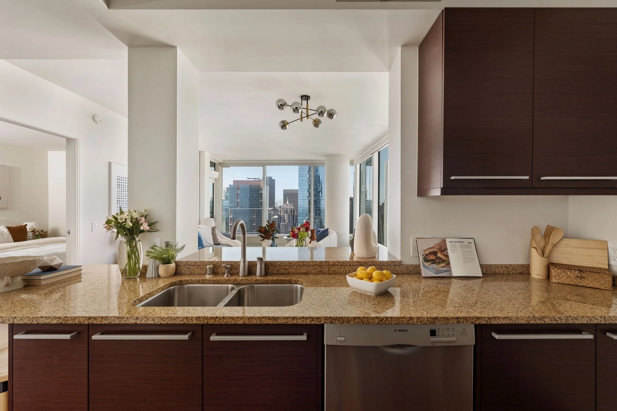 Modern kitchen with a granite countertop, flowers, lemons, and a view of a city skyline through large windows