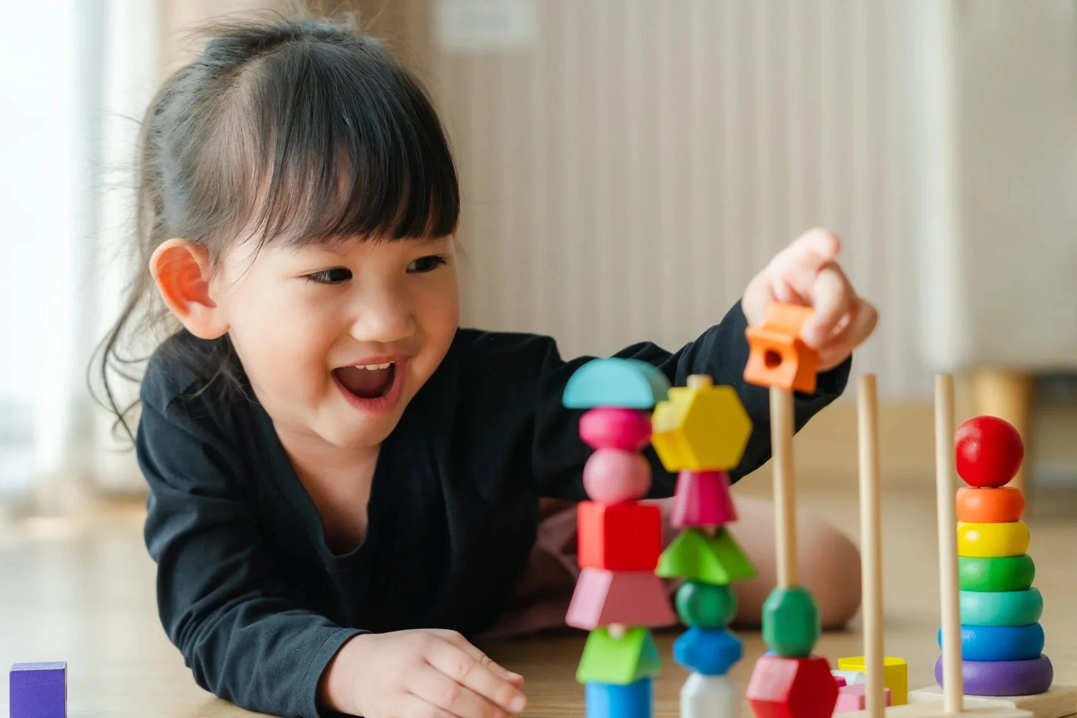 Smiling child playing with colorful wooden stacking toys and peg dolls, working on fine motor skills during occupational therapy for kids in Honolulu, HI