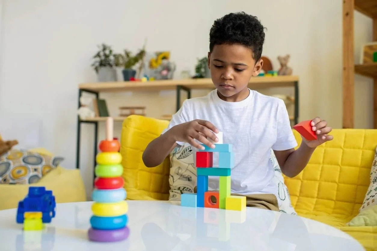 Young boy building a colorful block tower on a living room table, he is working on fine motor skills during in-home occupational therapy for kids in Honolulu, HI.