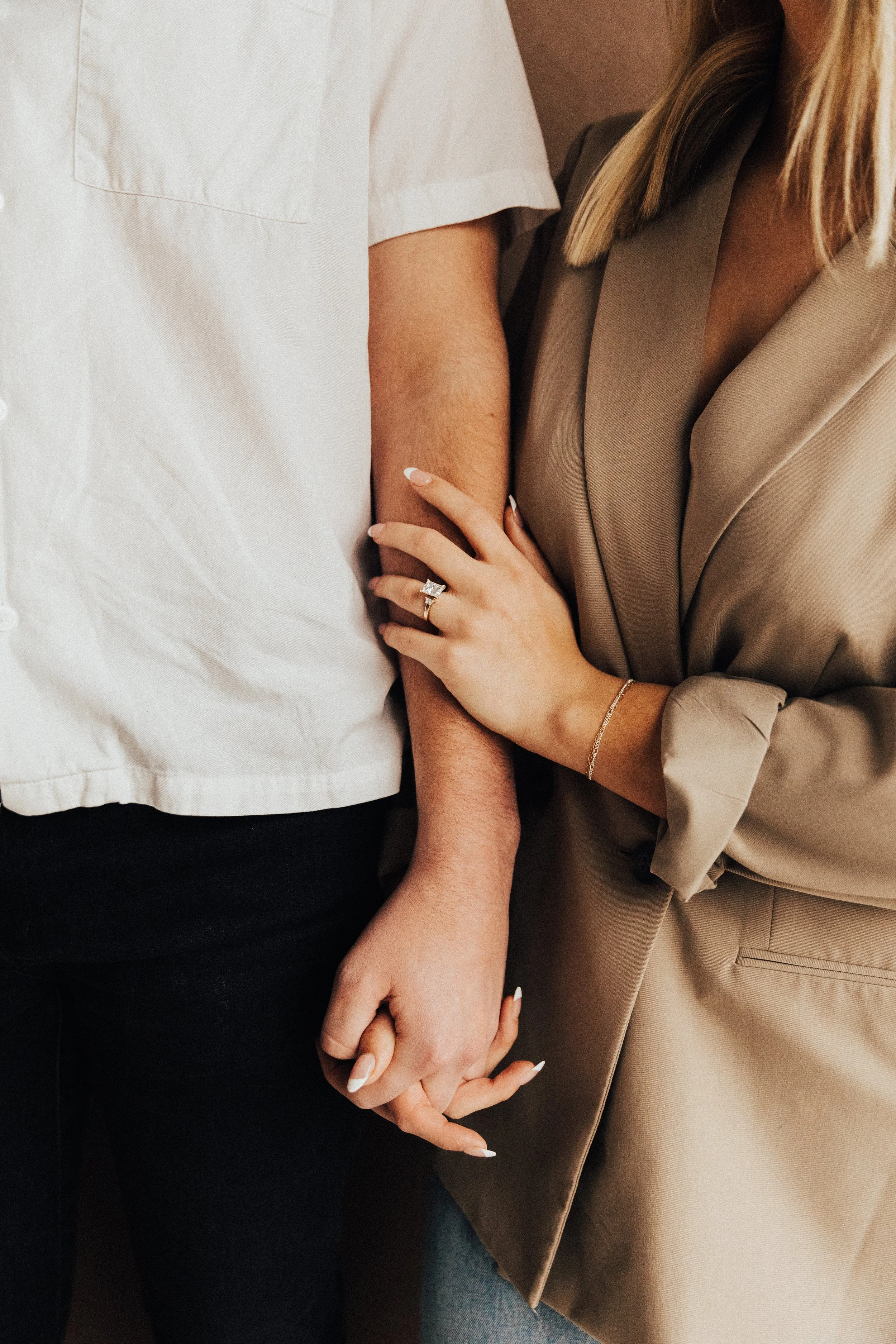 A close-up of two people holding hands, one wearing a ring, with both wearing professional or semi-formal clothing.