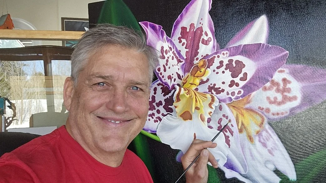 Bert Liverance smiling in a red shirt painting a large purple and white orchid on canvas