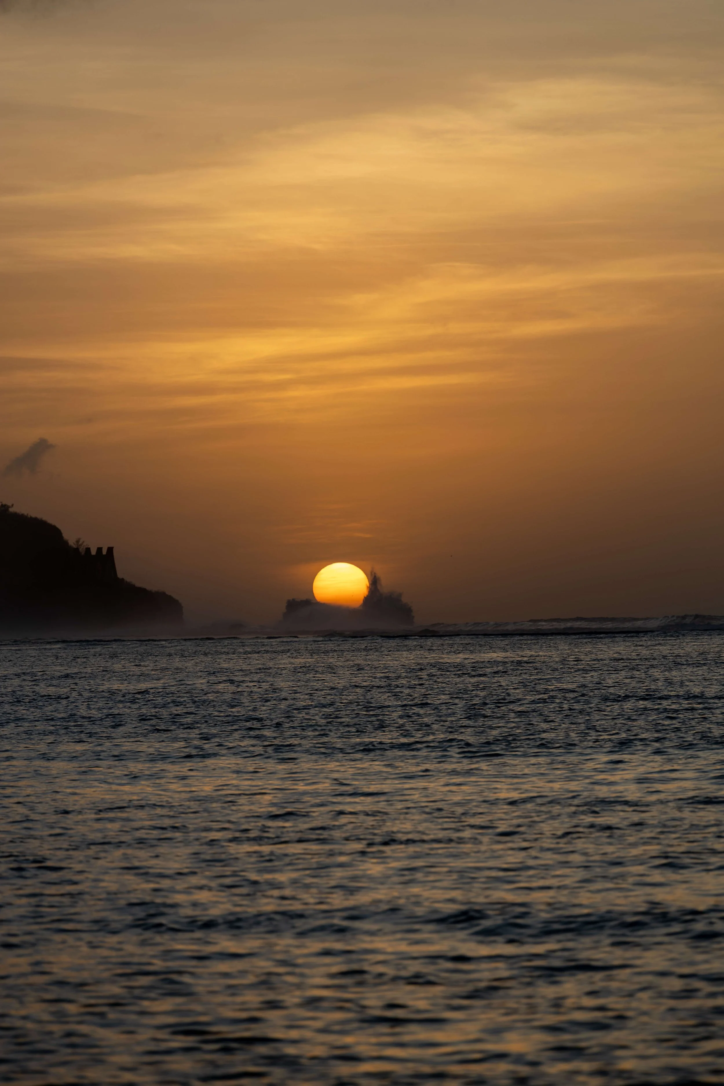 Sunset over the ocean with clouds and silhouettes of cliffs on the horizon.